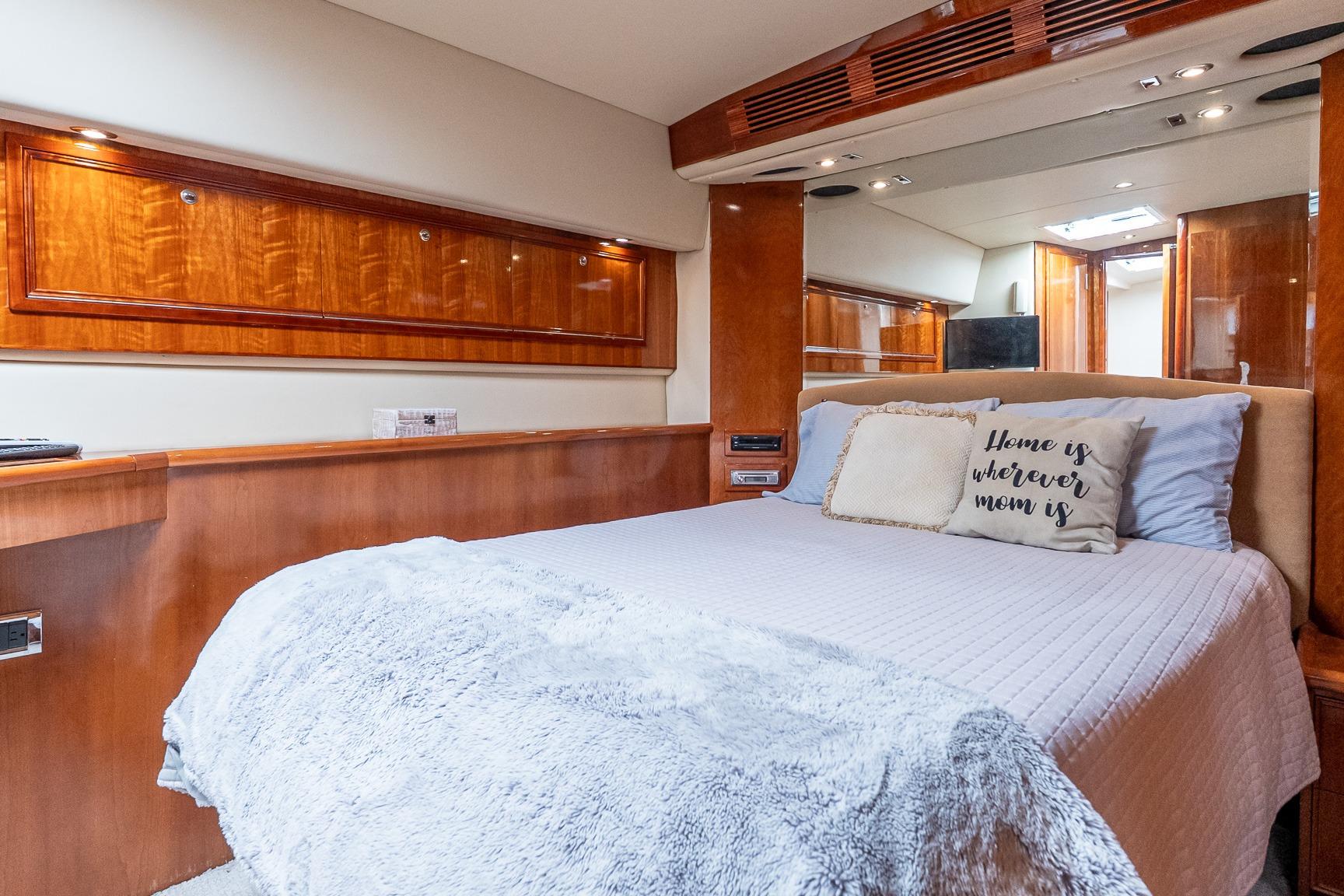 Luxurious 2005 Riviera 51 Flybridge yacht bedroom with cozy bedding and elegant wood finishes.