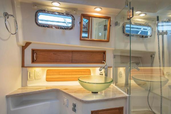 The image shows a sleek boat bathroom with a glass sink and wooden accents.