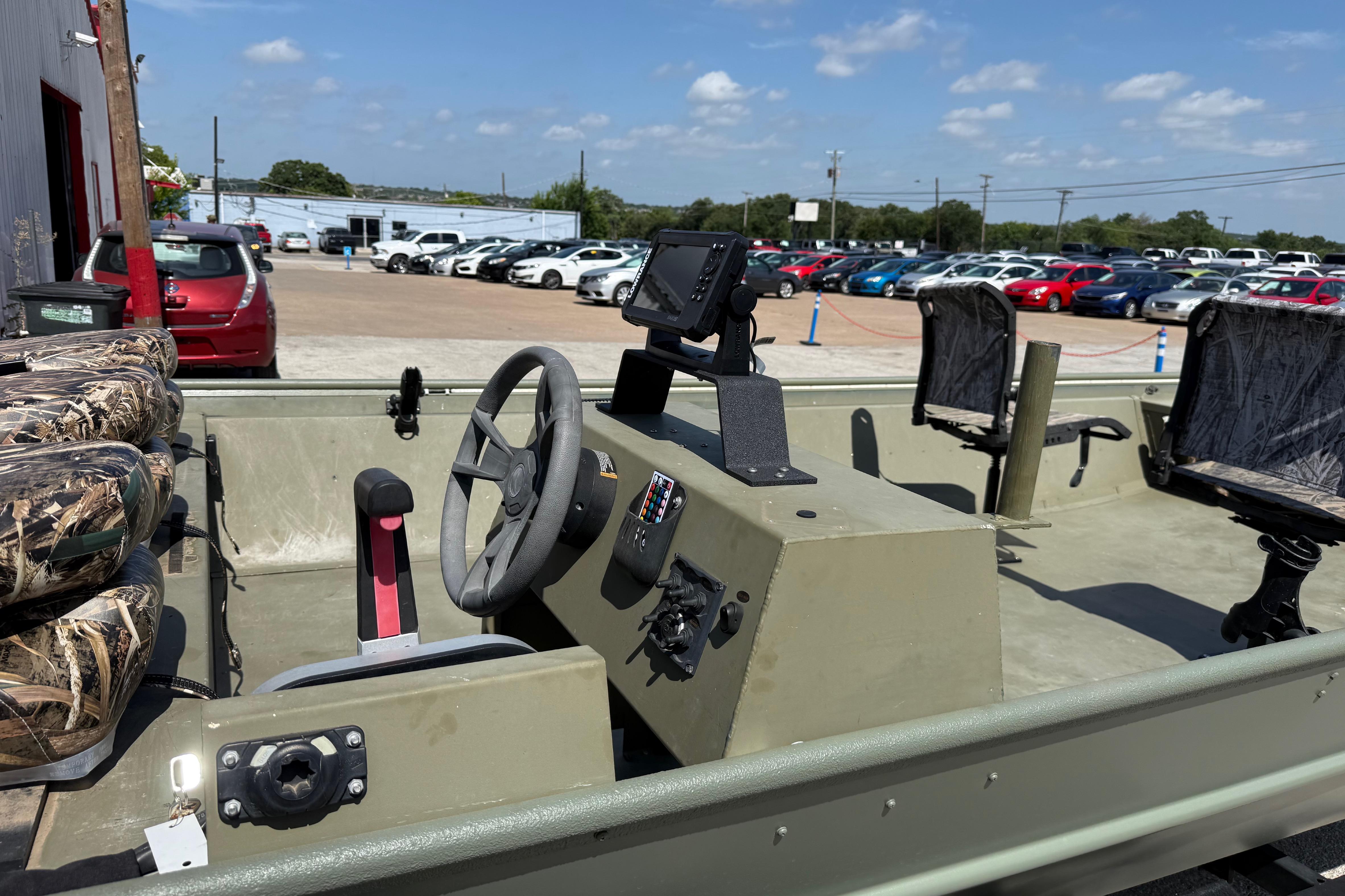 The image shows a 2020 Lowe Roughneck 2070 Big River boat. It features a sturdy, open design with a helm and several seats. Cars and a building are visible in the background.