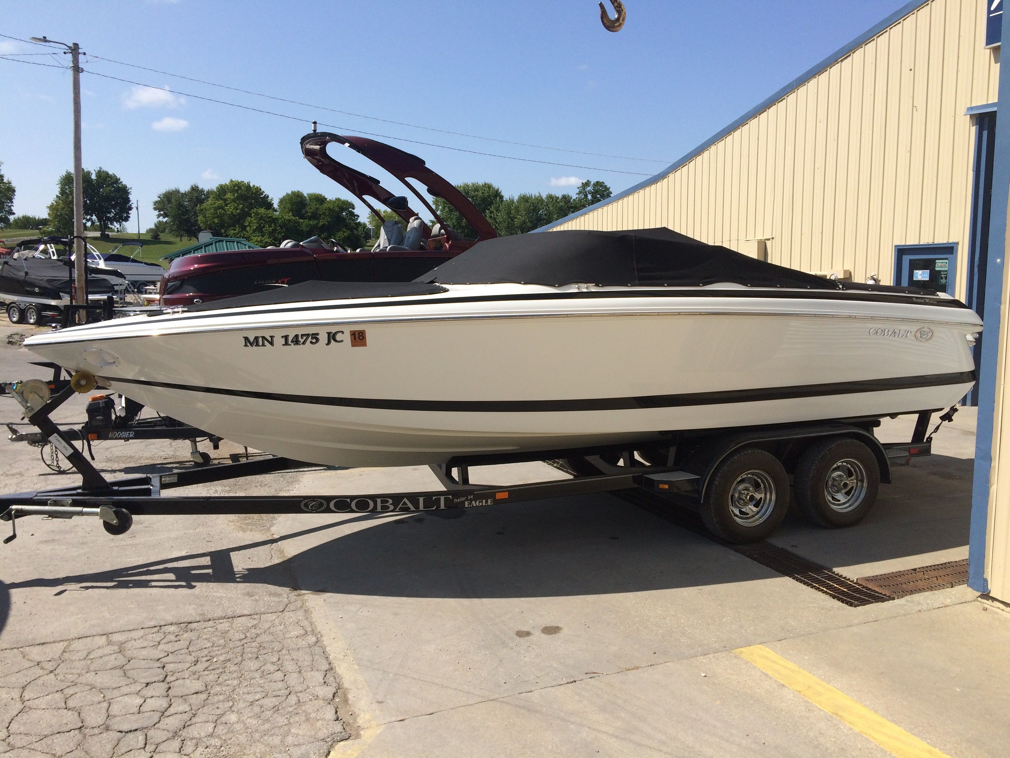 A white Cobalt boat on a trailer in front of a building.