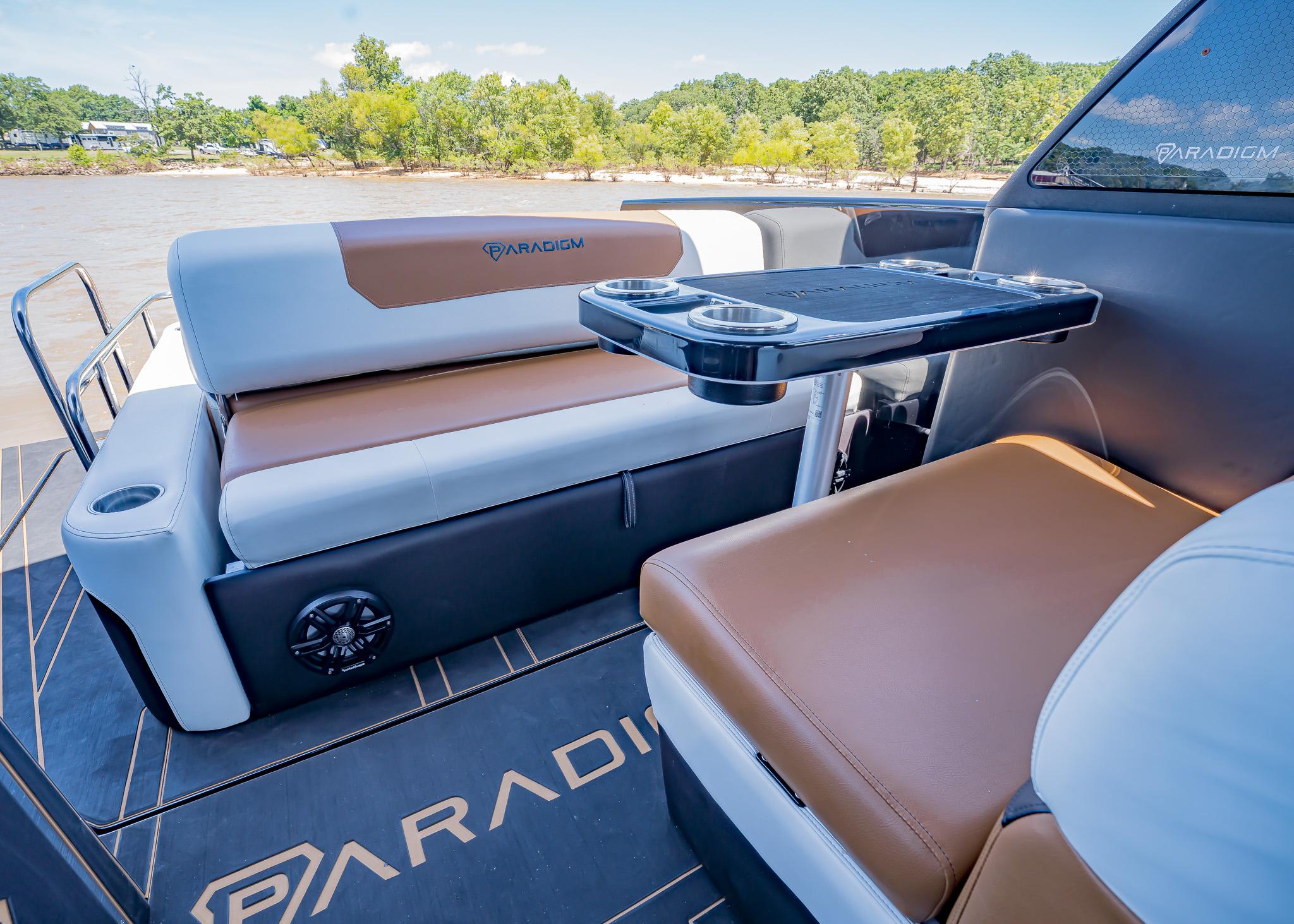 2025 Paradigm 236 boat interior with brown and white seating, cup holders, and scenic river view.