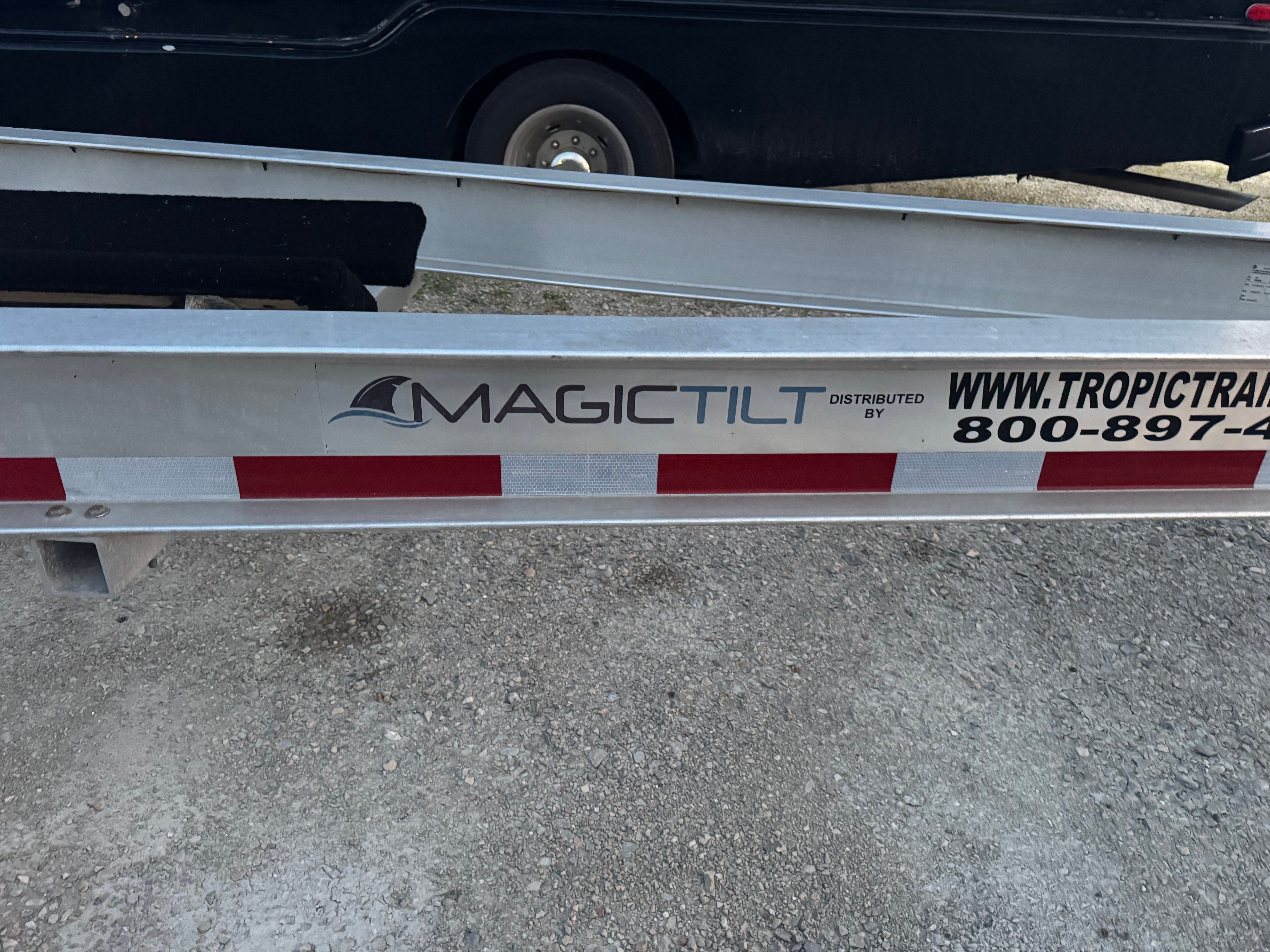 A boat trailer labeled "Magic Tilt" is on a gravel surface.