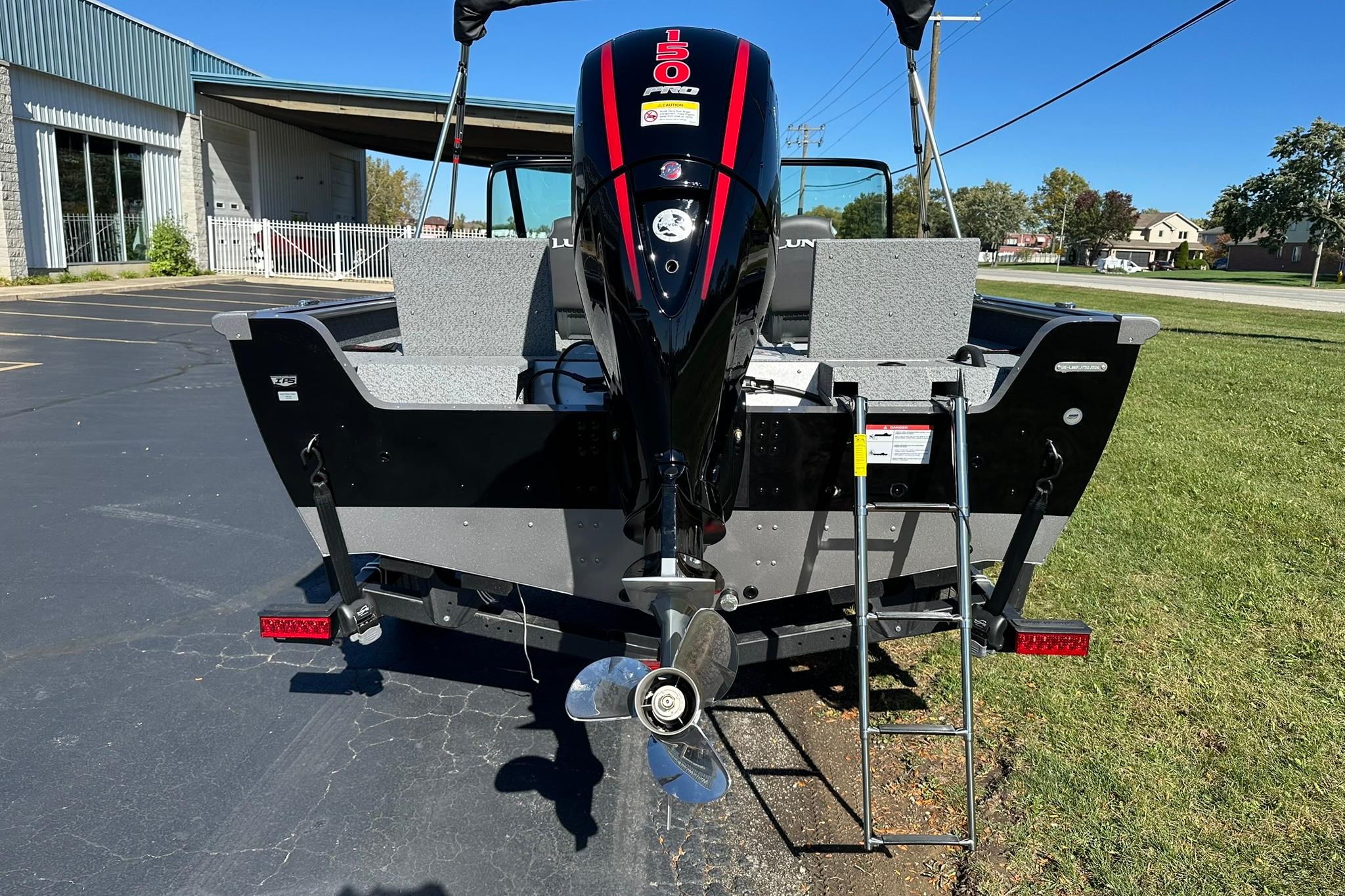 2026 Lund 1875 Impact XS Sport boat with outboard motor and ladder, parked outdoors.