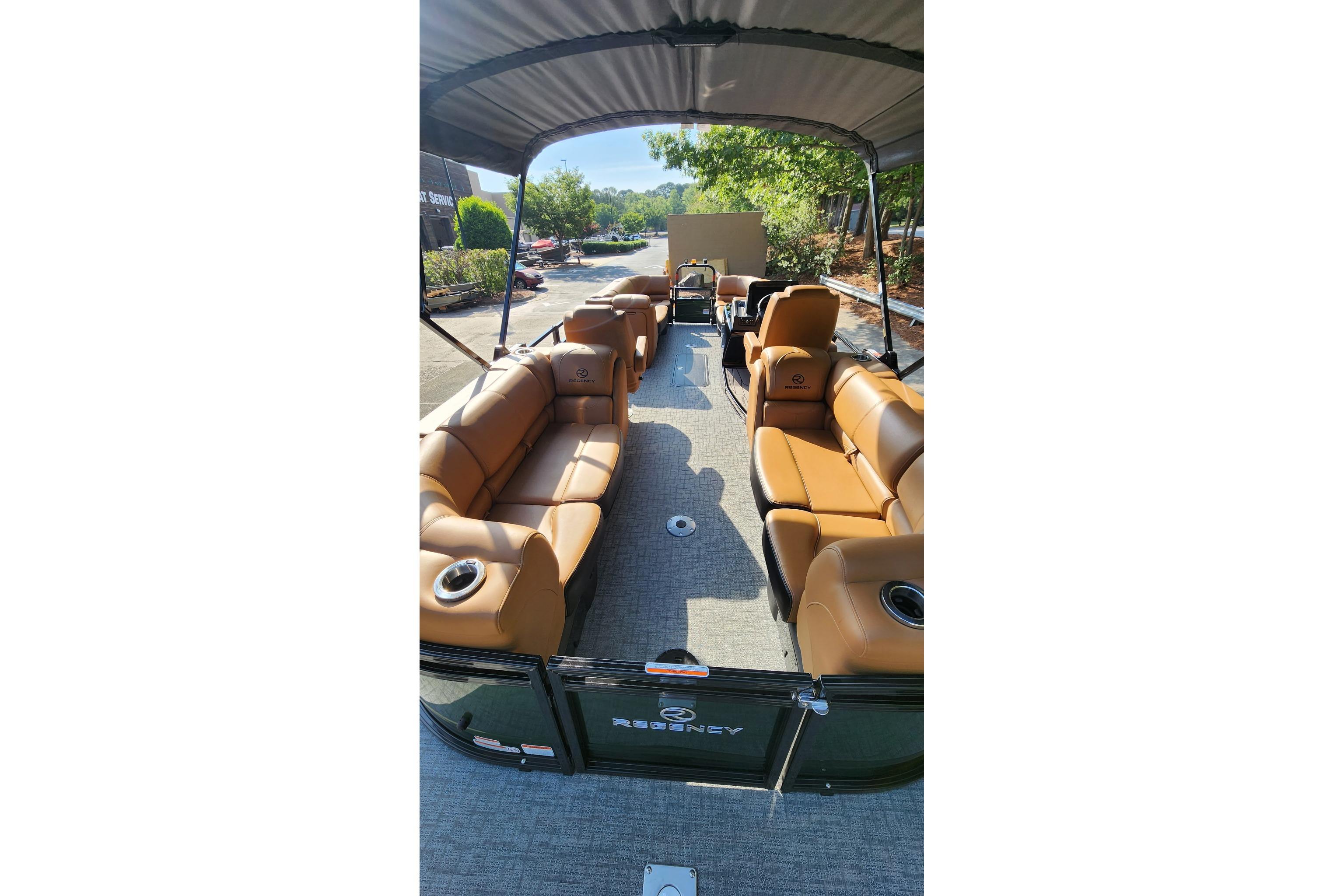 2026 Regency 230 DL pontoon boat with tan seating and canopy, parked outdoors.