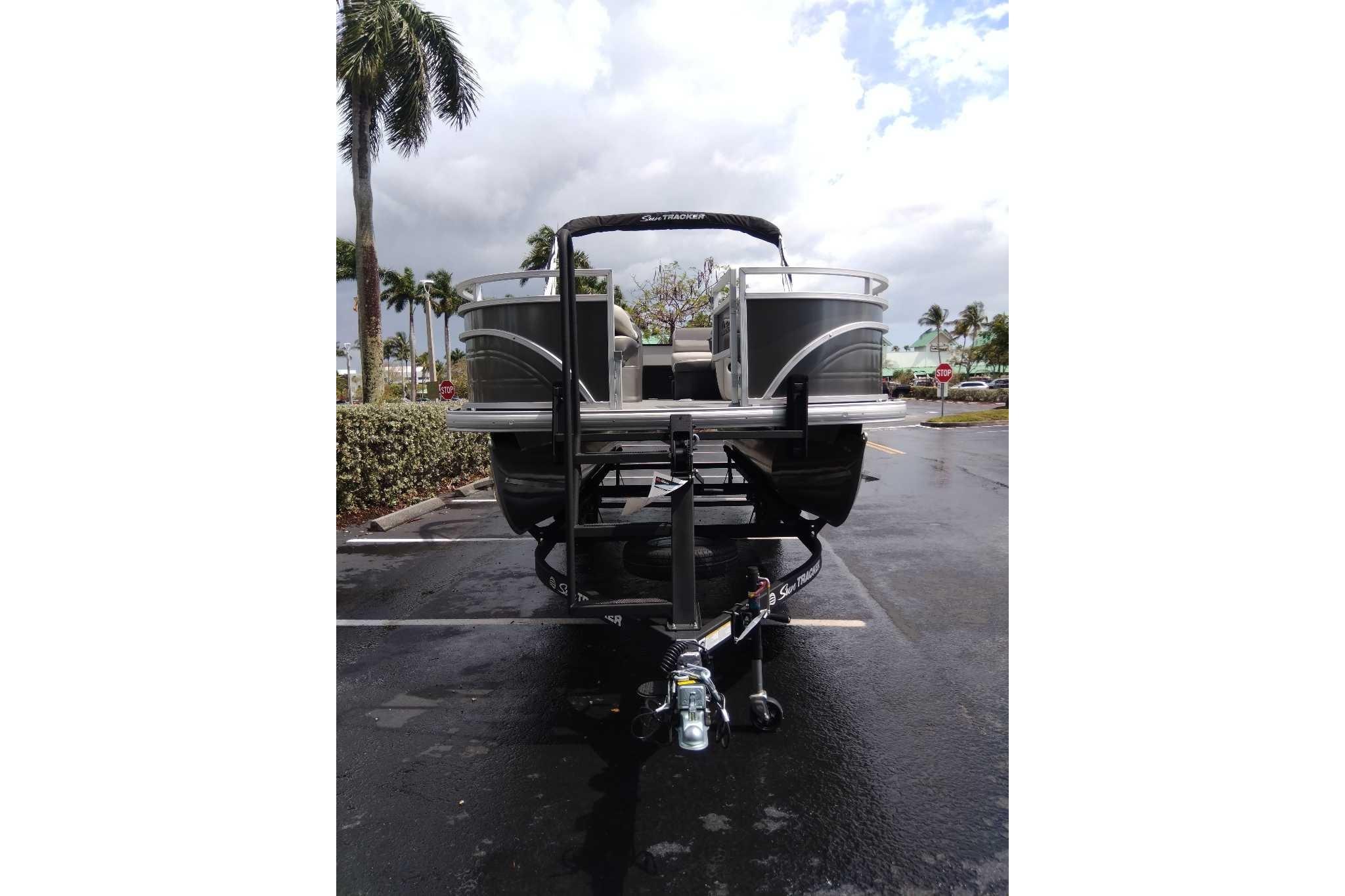 2026 Sun Tracker Fishin' Barge 22 DLX pontoon boat on trailer in parking lot.