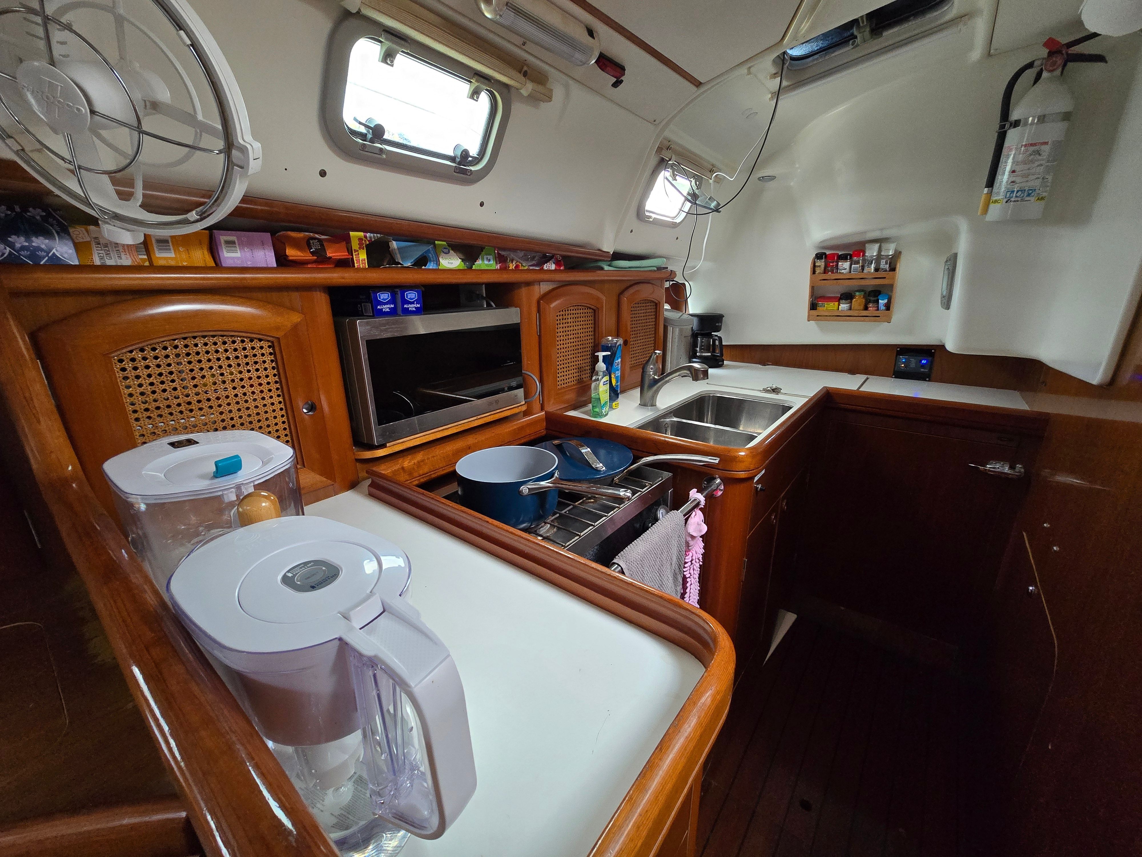 The galley of a 1998 Beneteau 411 with wooden cabinets, sink, and cooking utensils.