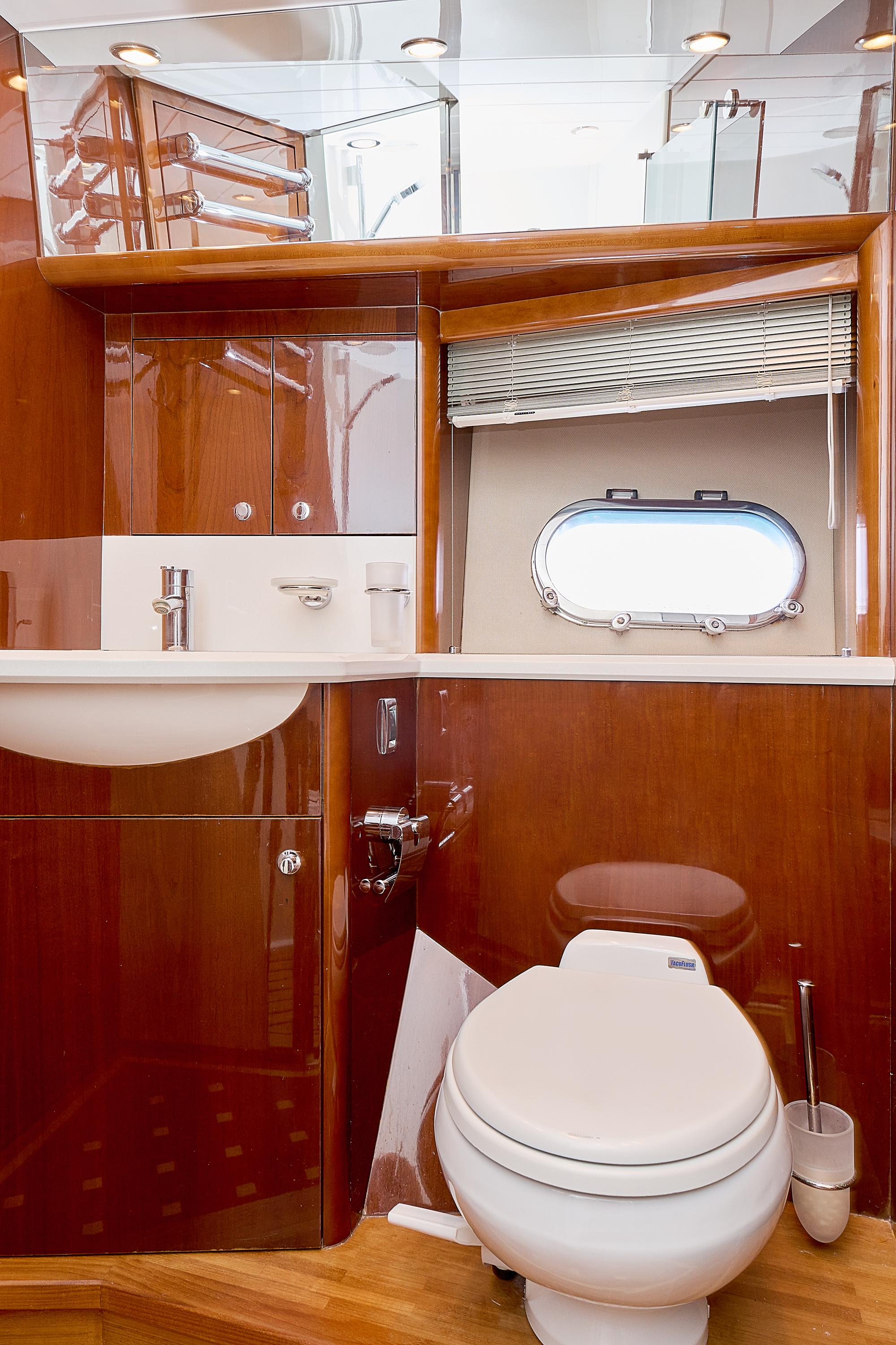 Luxurious yacht bathroom with wooden cabinetry, sink, and porthole window in a 2009 Princess 23M.