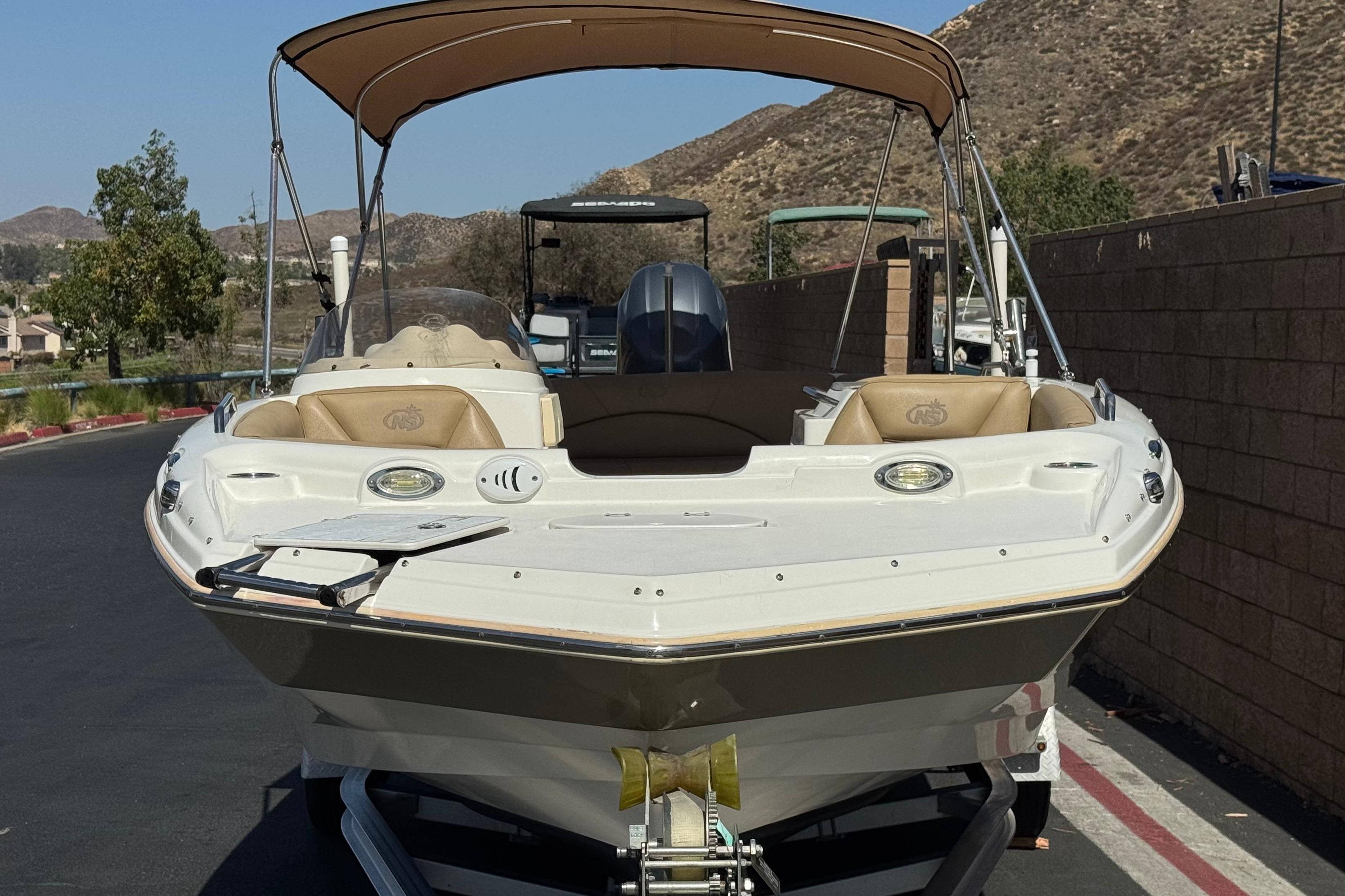 2020 NauticStar 203 SC boat on trailer, parked near a brick wall and scenic hills.