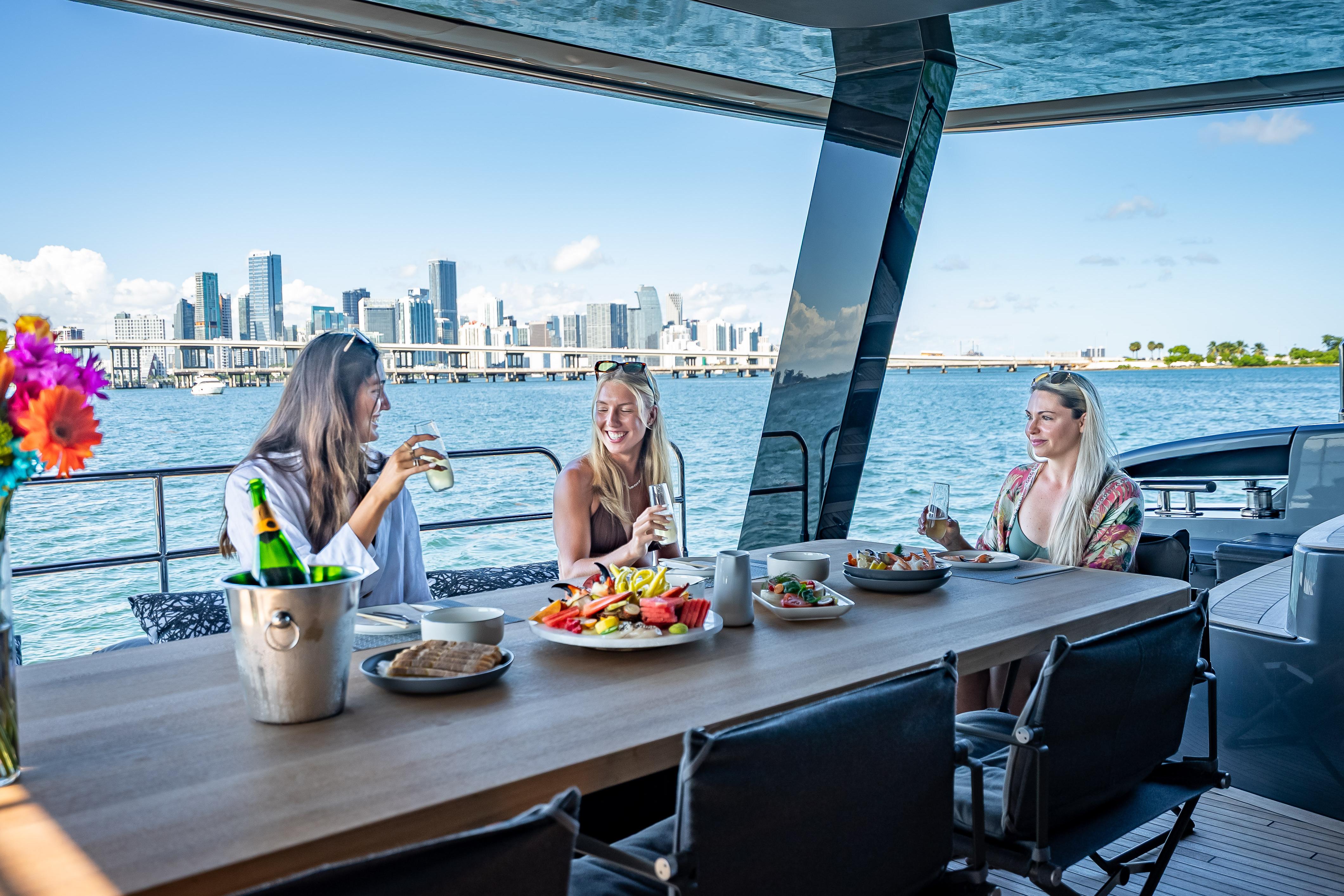 Women enjoying a meal on a 2026 Sunreef 60 Power yacht with city skyline view.