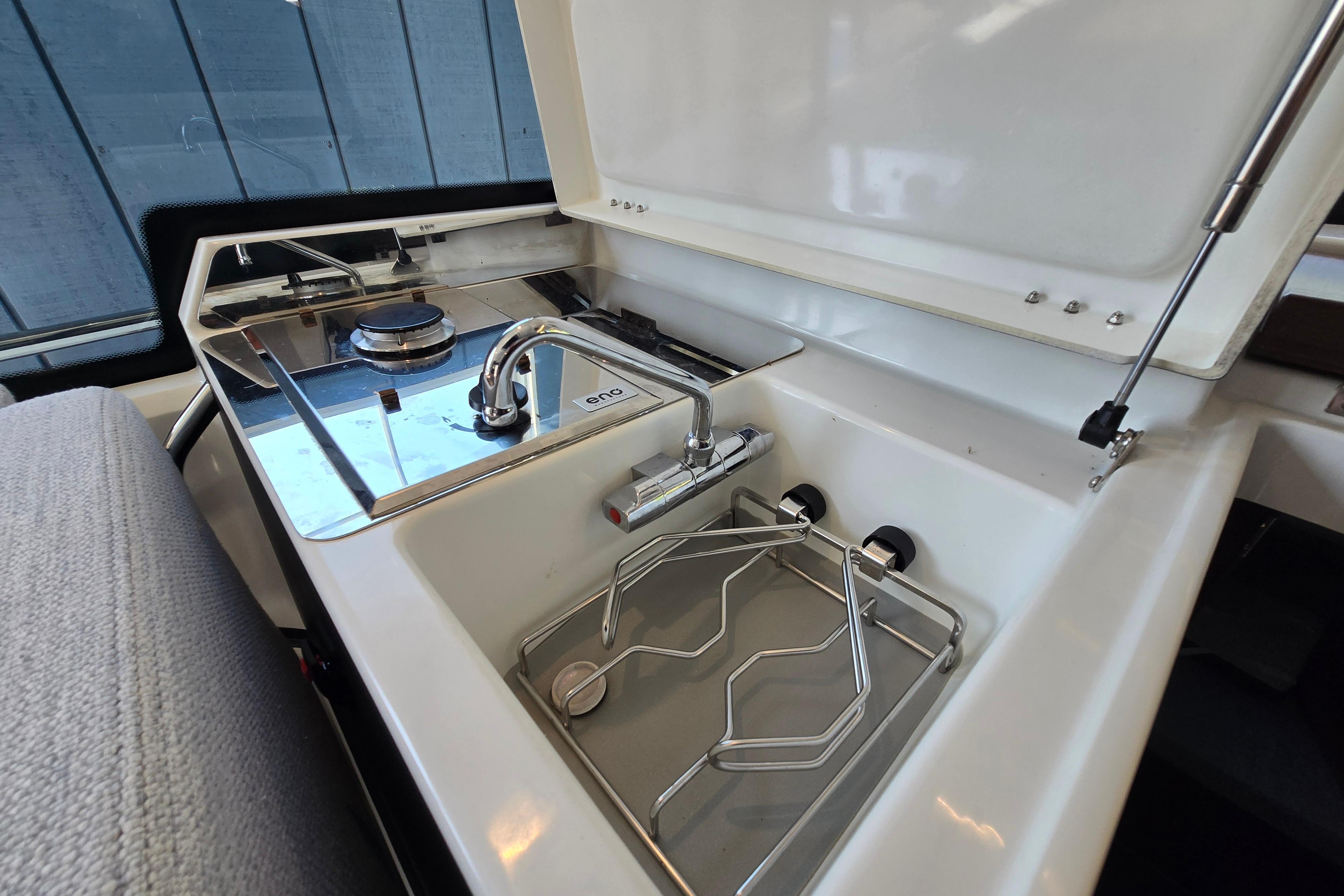 Compact kitchenette with sink, stove, and storage in a modern boat.