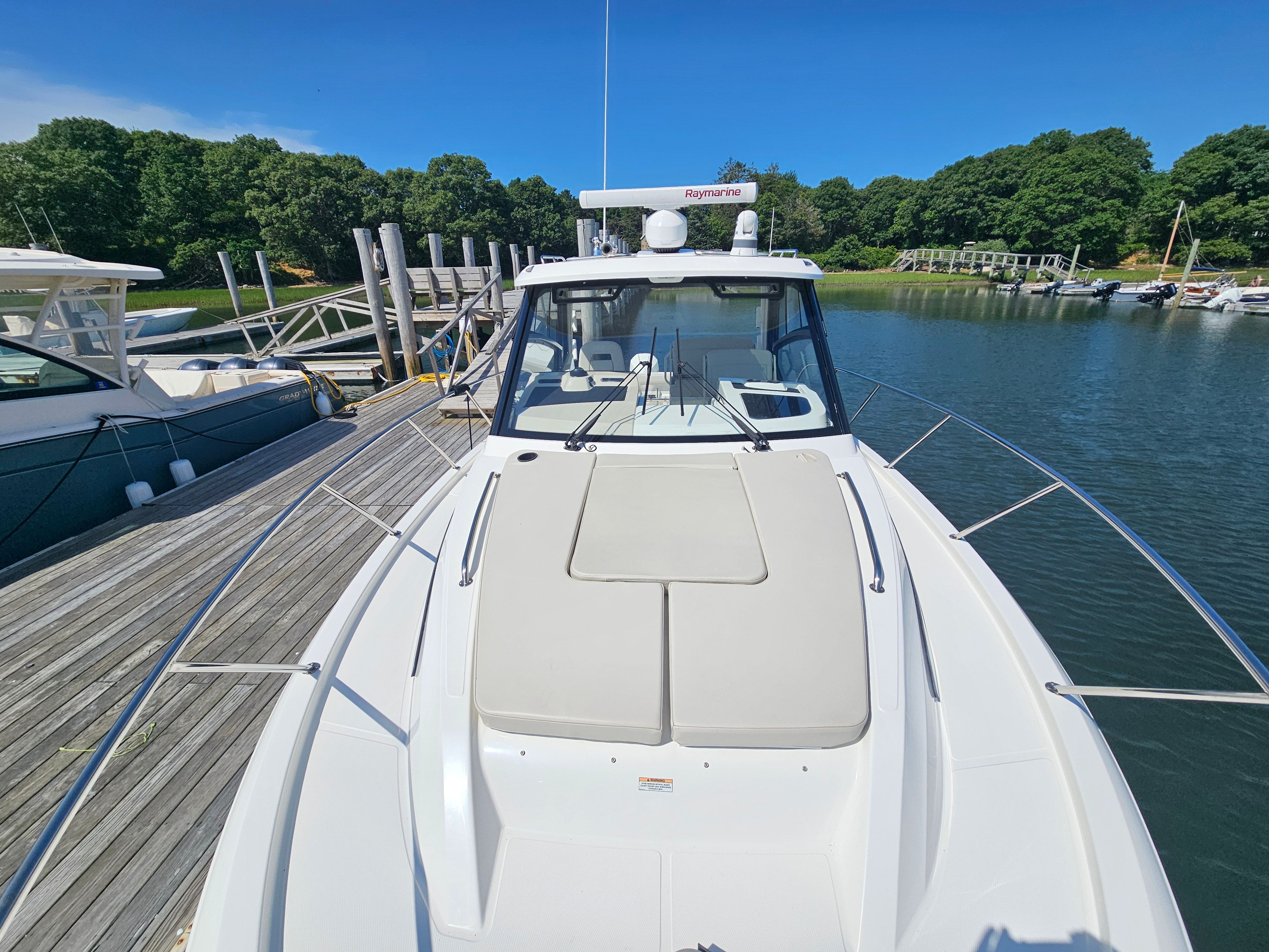 A 2023 Boston Whaler 325 Conquest docked at a wooden pier in a calm harbor.