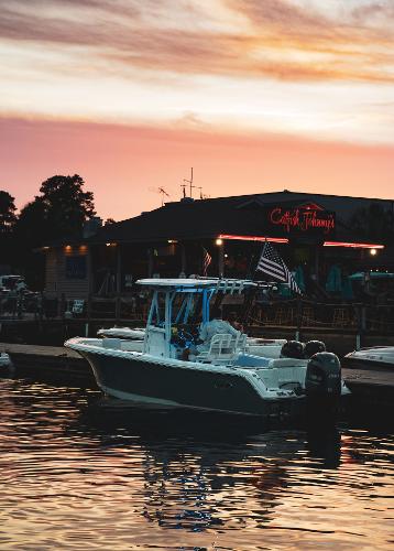 2024 Sea Hunt Ultra 234 boat docked at sunset near a waterfront restaurant.