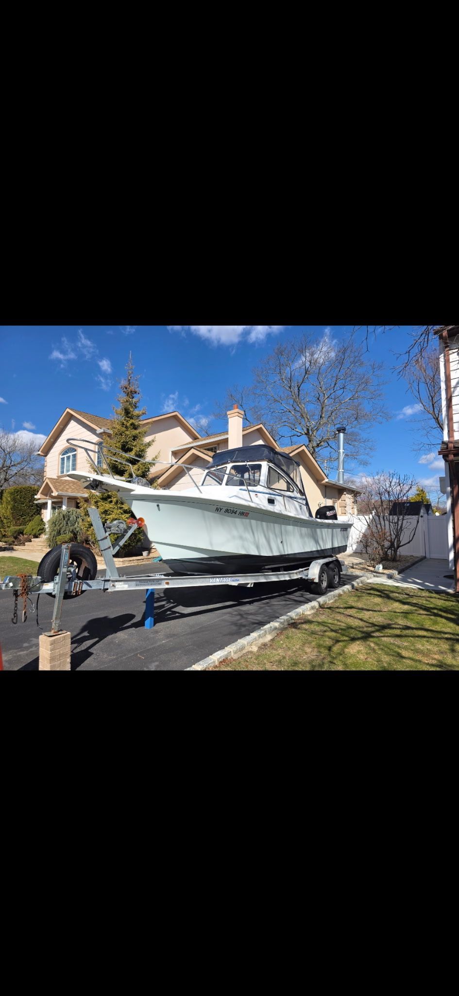 A boat on a trailer in front of a house, surrounded by trees.