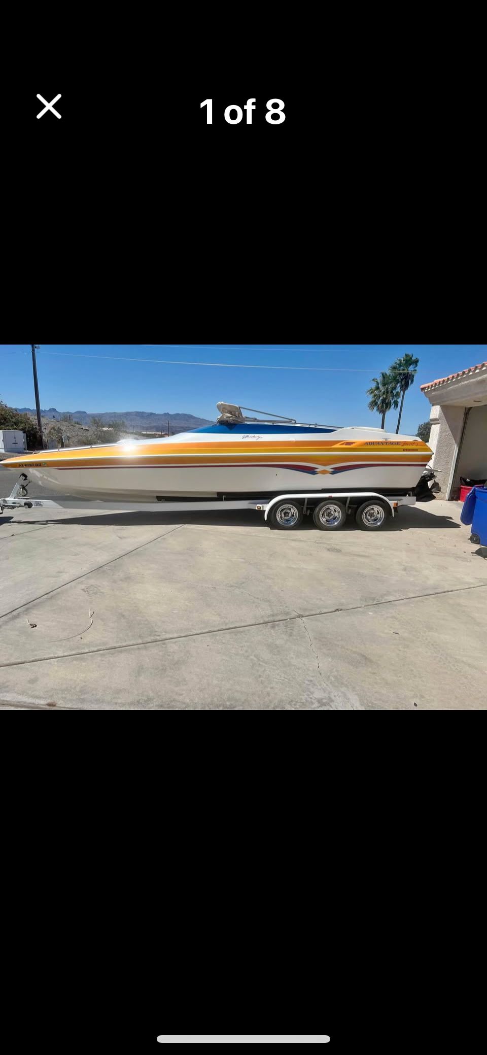 A white boat with a yellow cover sits on a trailer in a driveway.