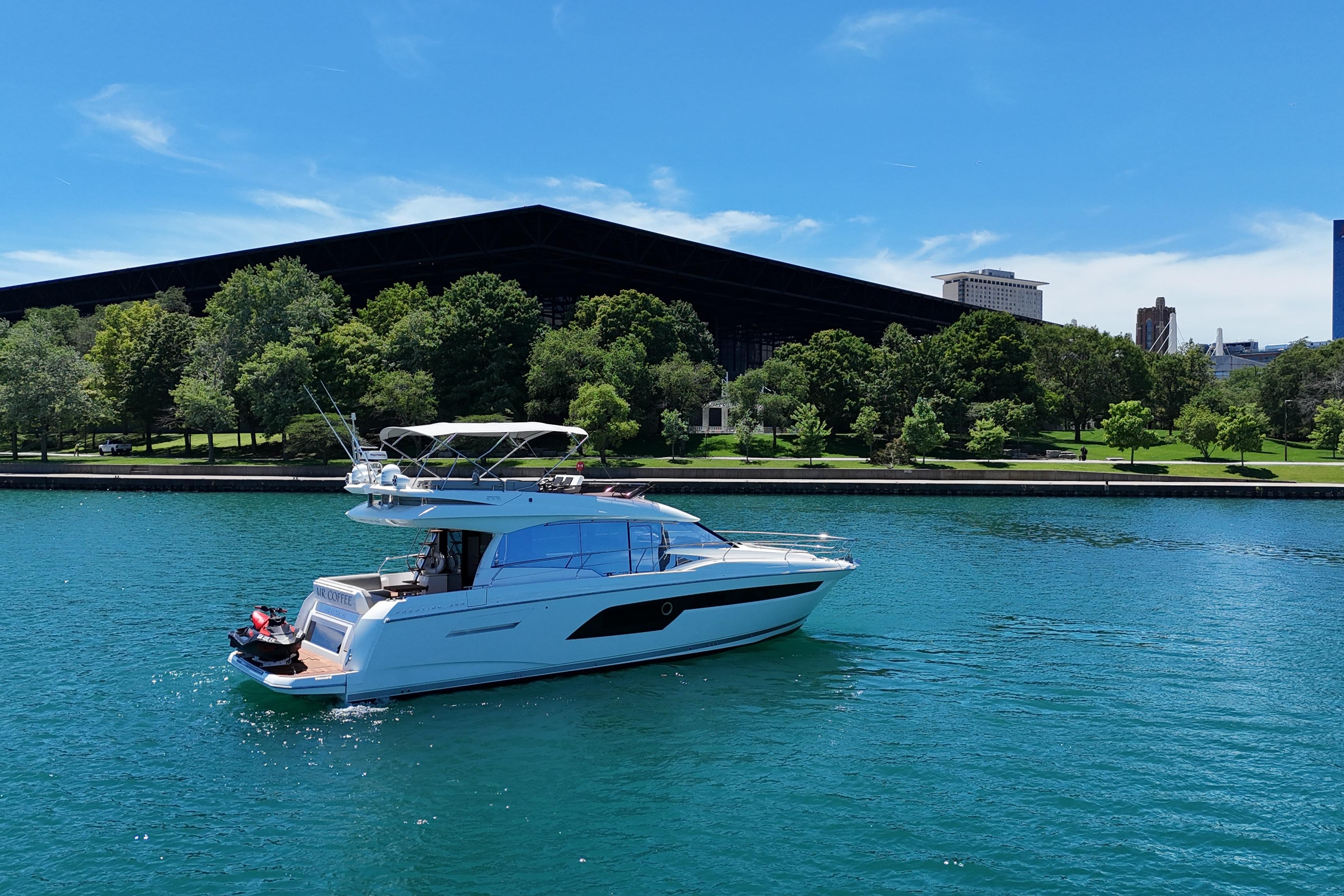 2022 Prestige 520 yacht cruising on a serene blue lake near a lush green park.