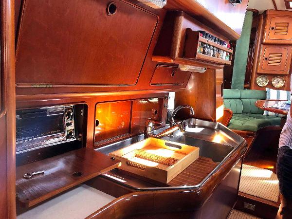 Interior view of a yacht kitchen with wood paneling, sink, and oven. Green sofa in the background.