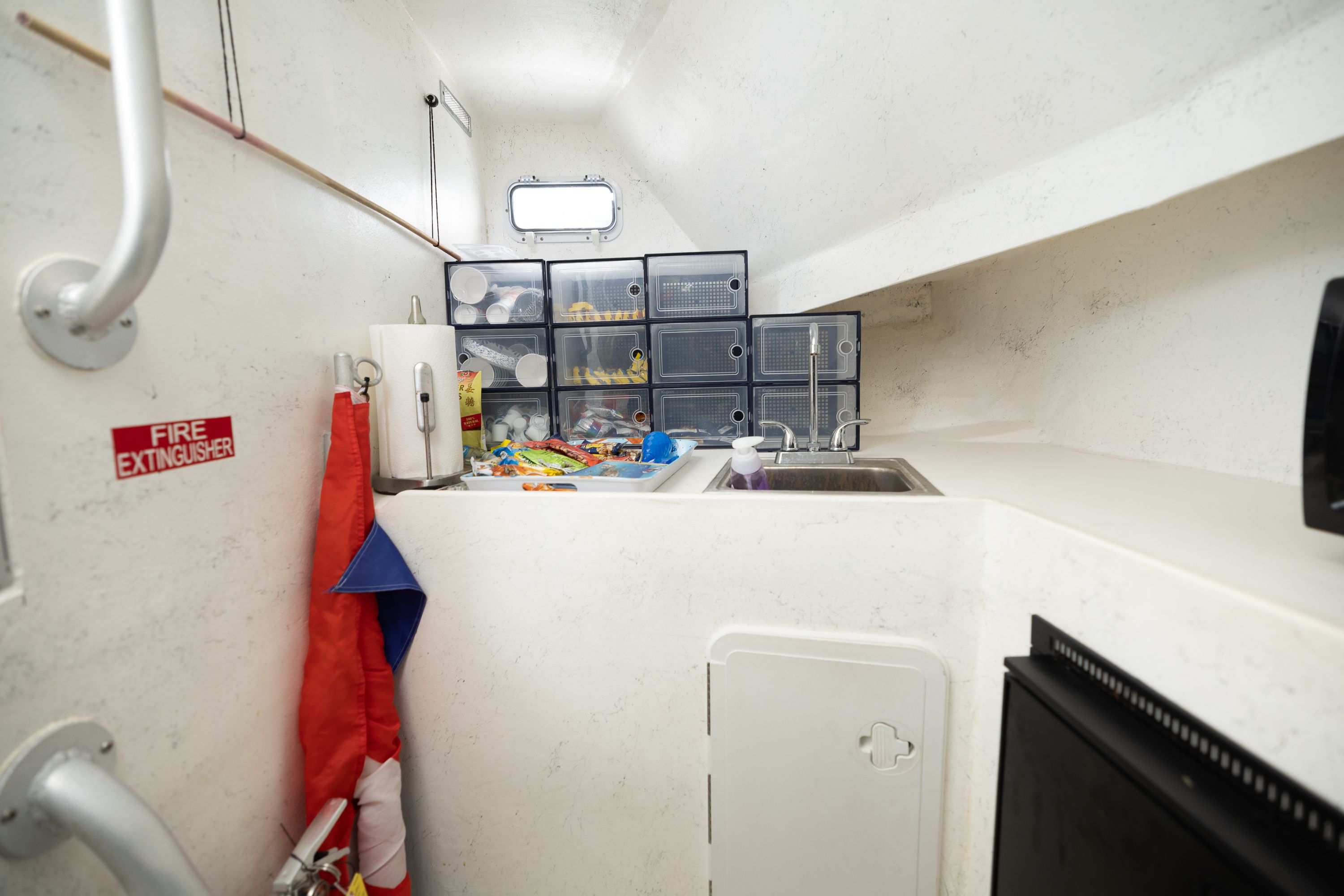 Interior of a boat with a sink, storage bins, and a fire extinguisher.