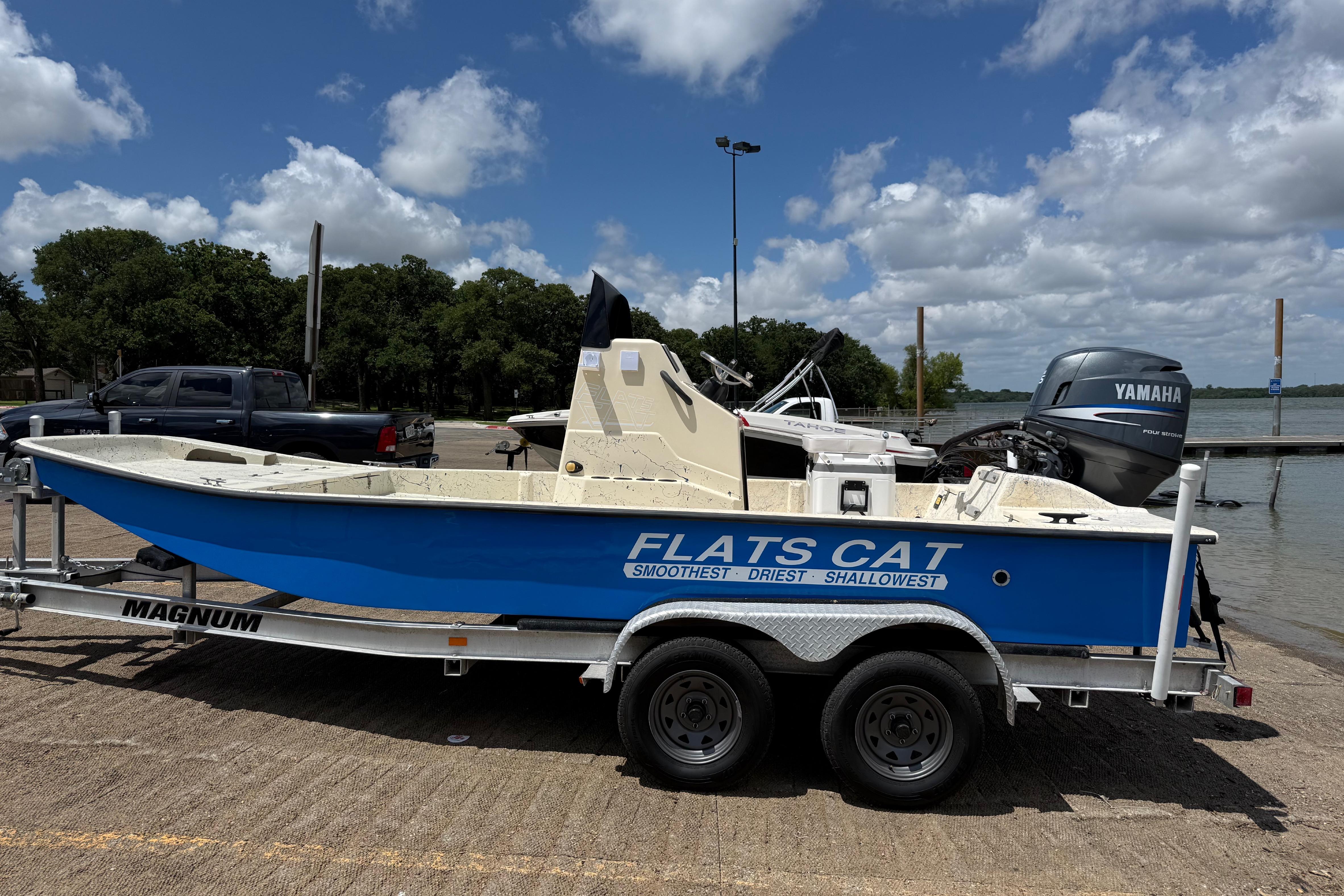 Blue 2007 Flats Cat 19 boat on trailer, parked near a lake under a cloudy sky.