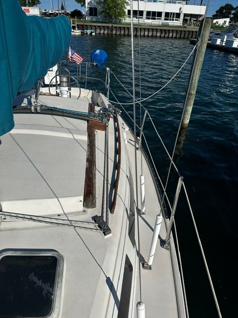A 1985 Catalina 27 sailboat on the water, featuring a blue sail and wooden railing.