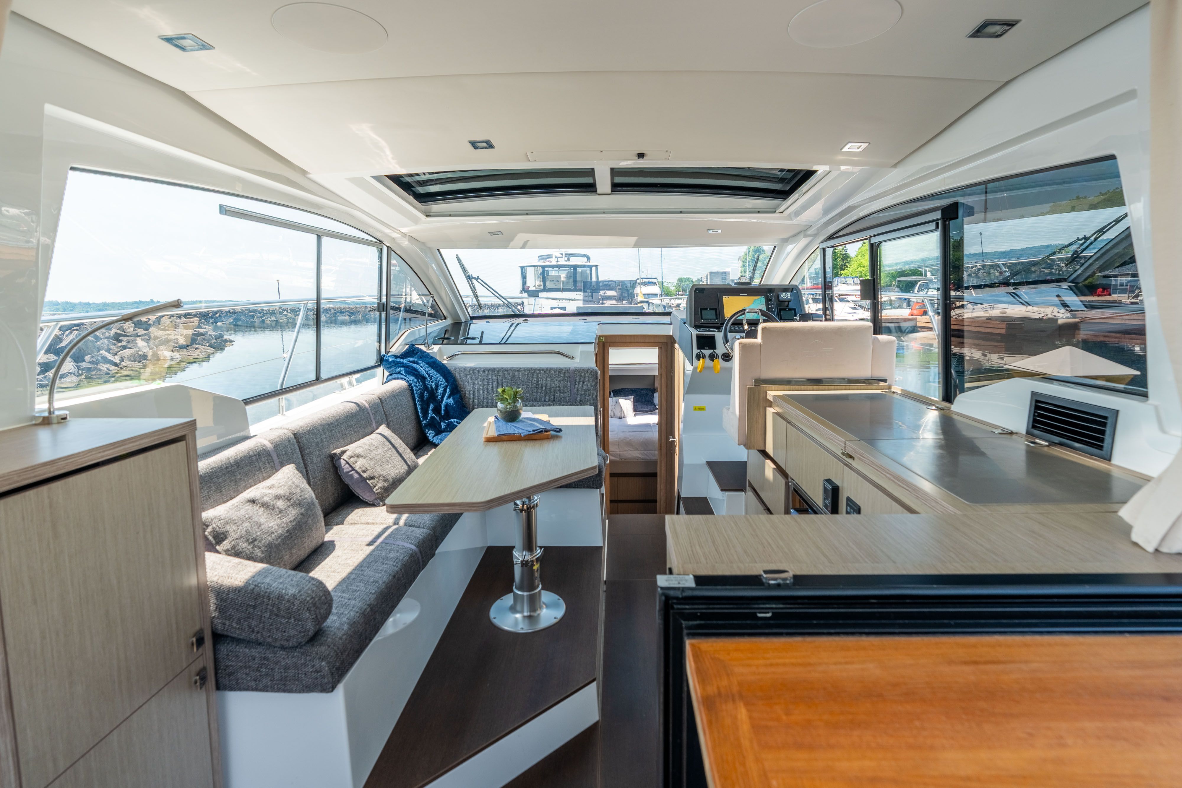 Interior of a modern yacht with seating area, table, and kitchenette, overlooking the water.
