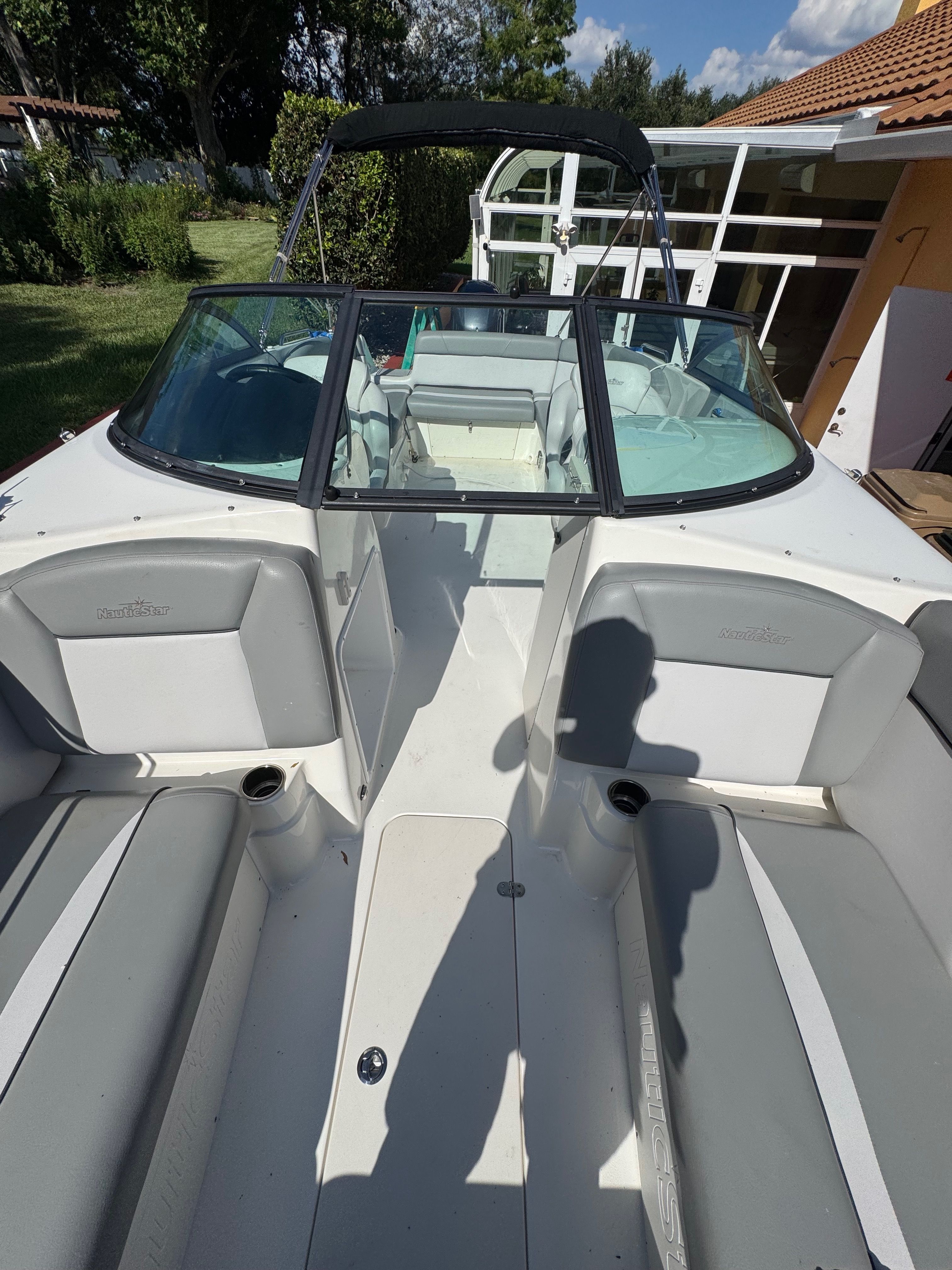 The image shows the cockpit of a NauticStar 243 DC boat with gray seating and a black bimini top.