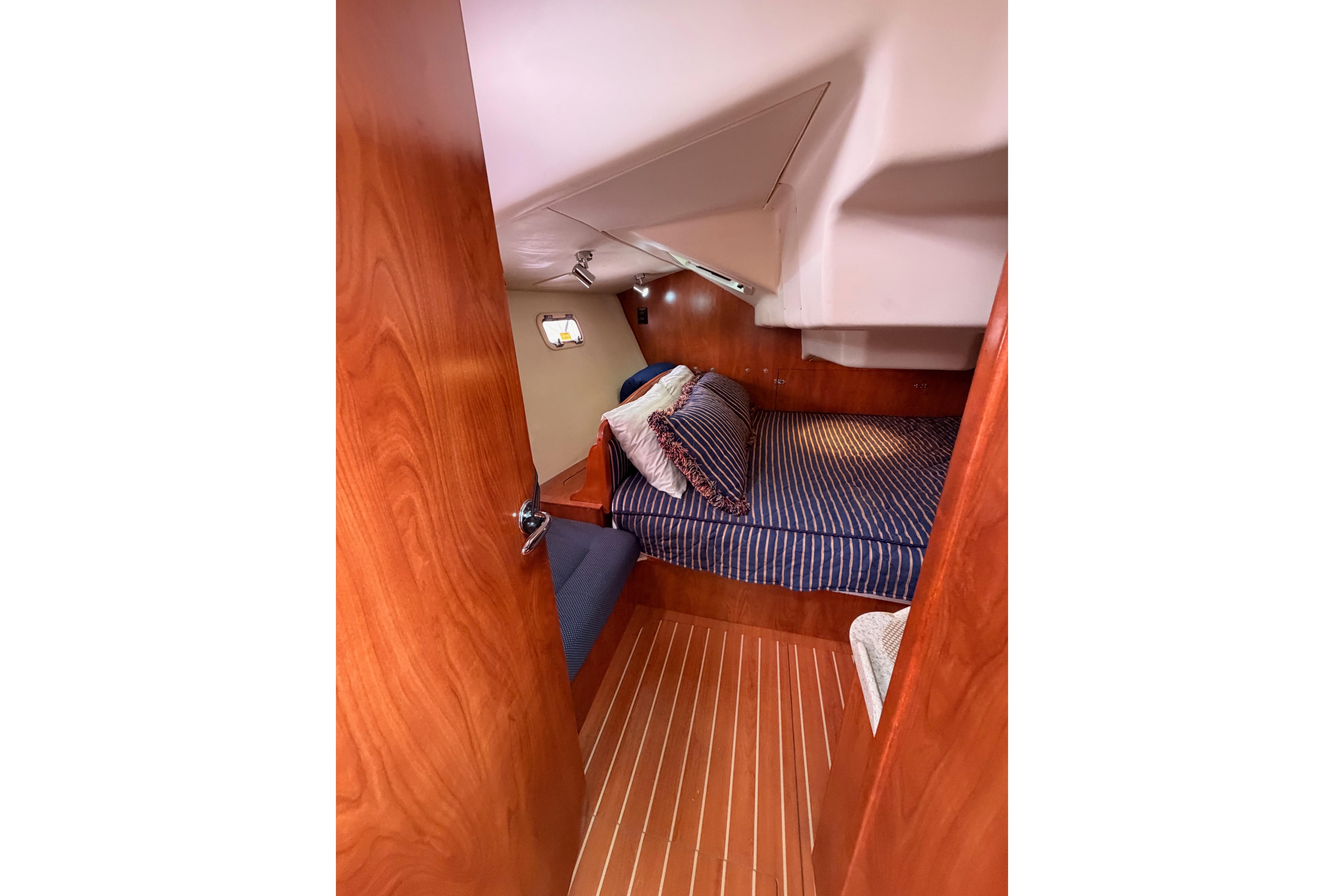 Cozy cabin interior of 2009 Hunter 38 sailboat with striped bedding and wooden finishes.
