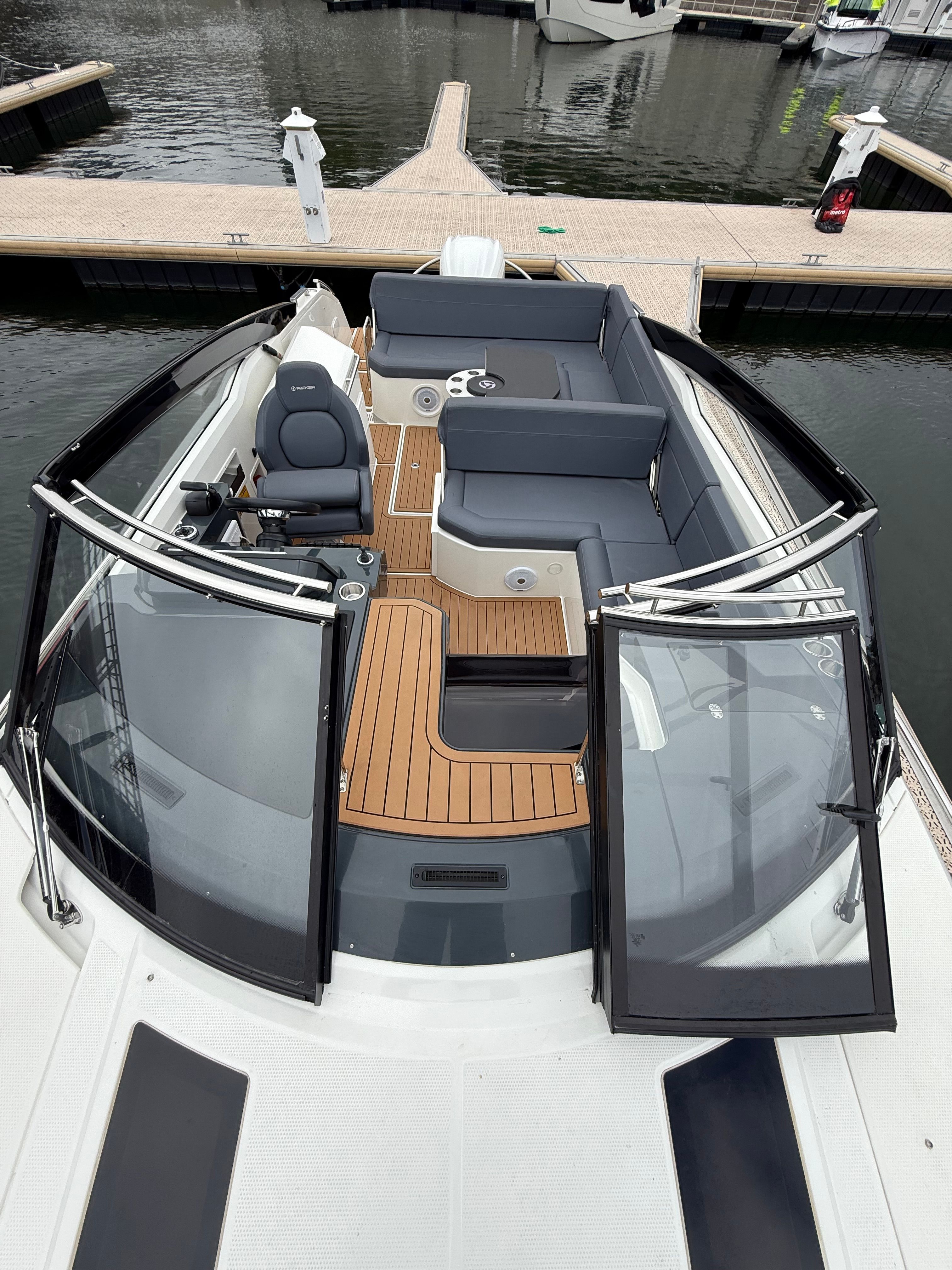 A modern motorboat with sleek seating and wooden flooring, docked in a calm marina.
