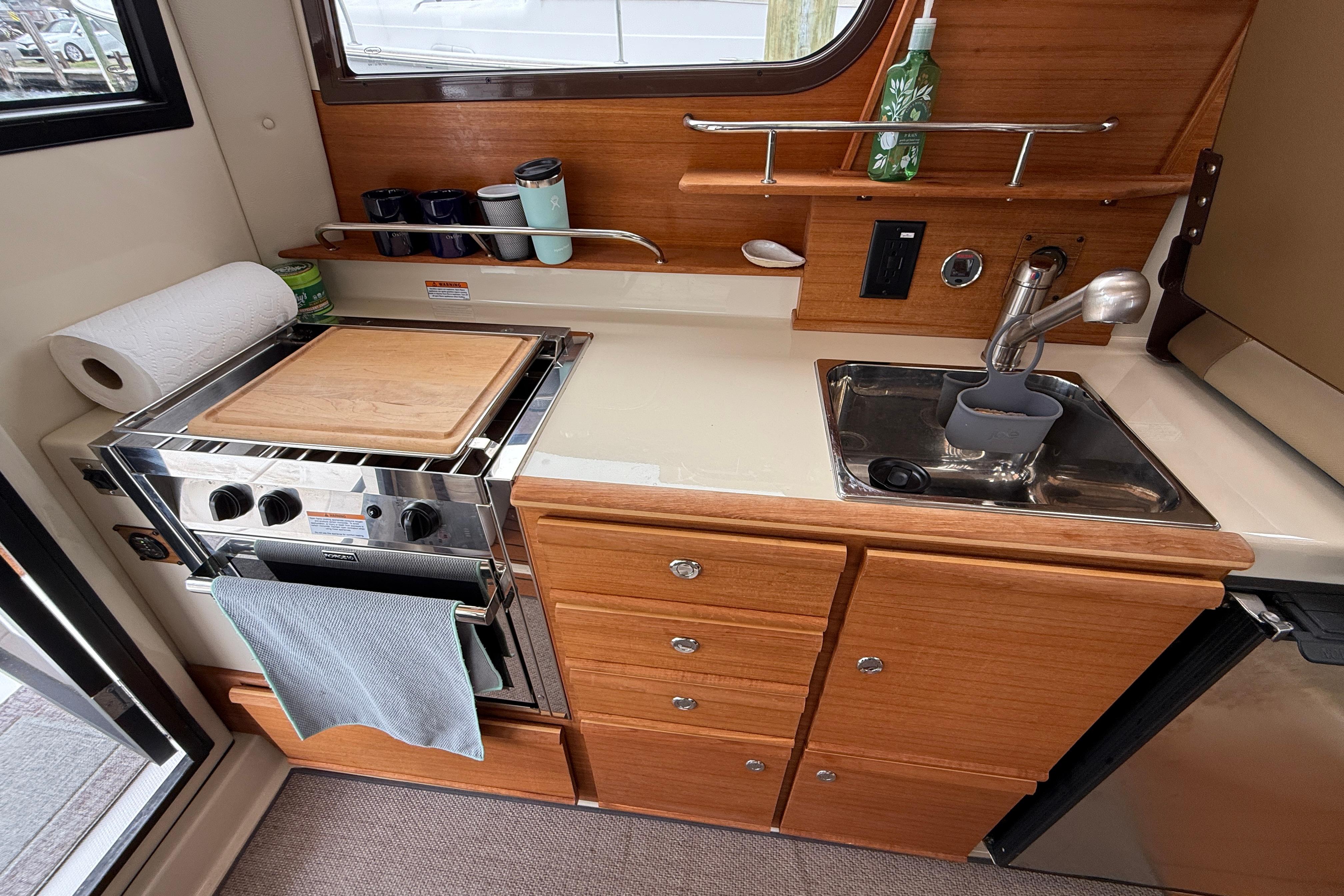 2024 Ranger Tugs R-27 galley with stove, sink, and wooden cabinetry.