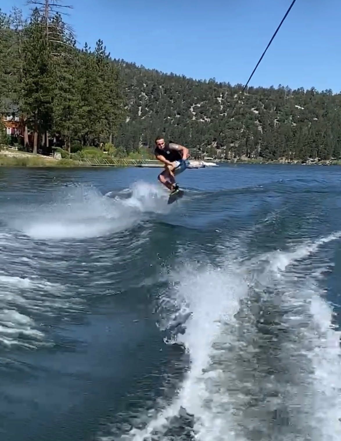 Wakeboarder jumps behind MasterCraft NXT22 on a lake.