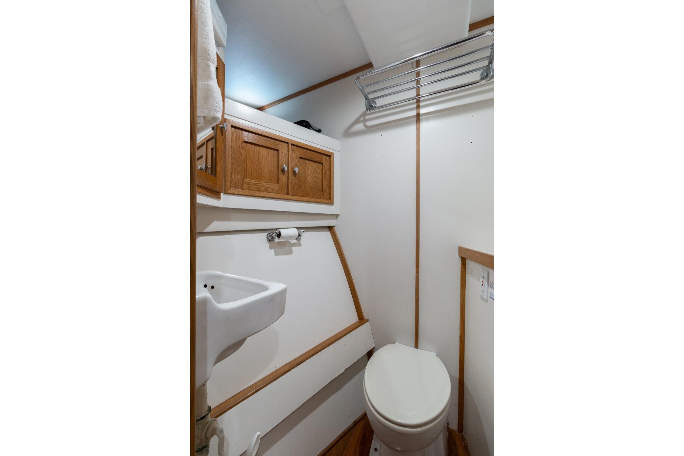 Compact bathroom in 1963 Trumpy Classic boat with wooden cabinets and white fixtures.