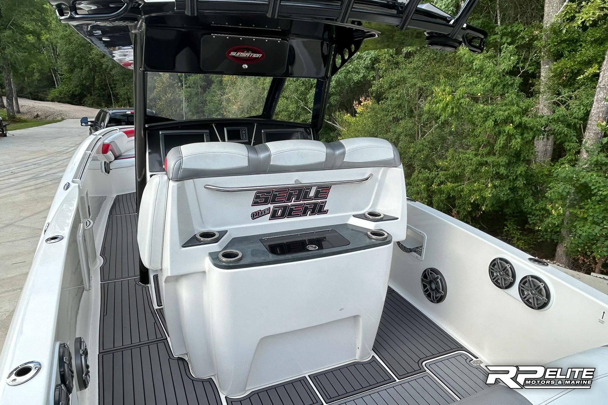 2013 Sunsation 34 CCX boat interior with seating and cup holders, surrounded by lush greenery.