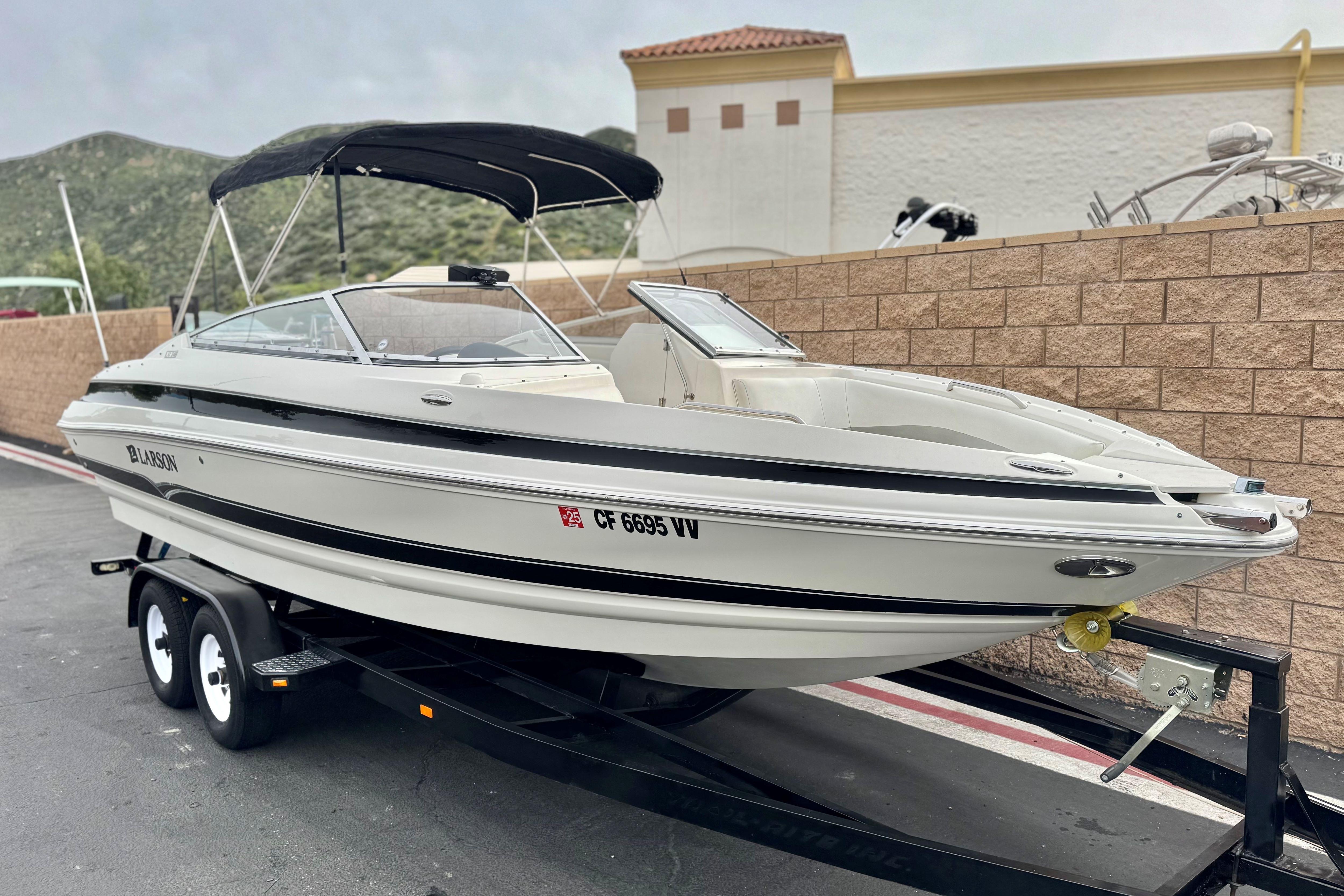 2006 Larson LXi 248 boat on trailer, parked outdoors with mountains in background.
