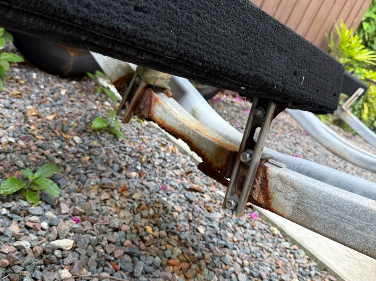 Close-up of a boat trailer with rusty metal parts on gravel.