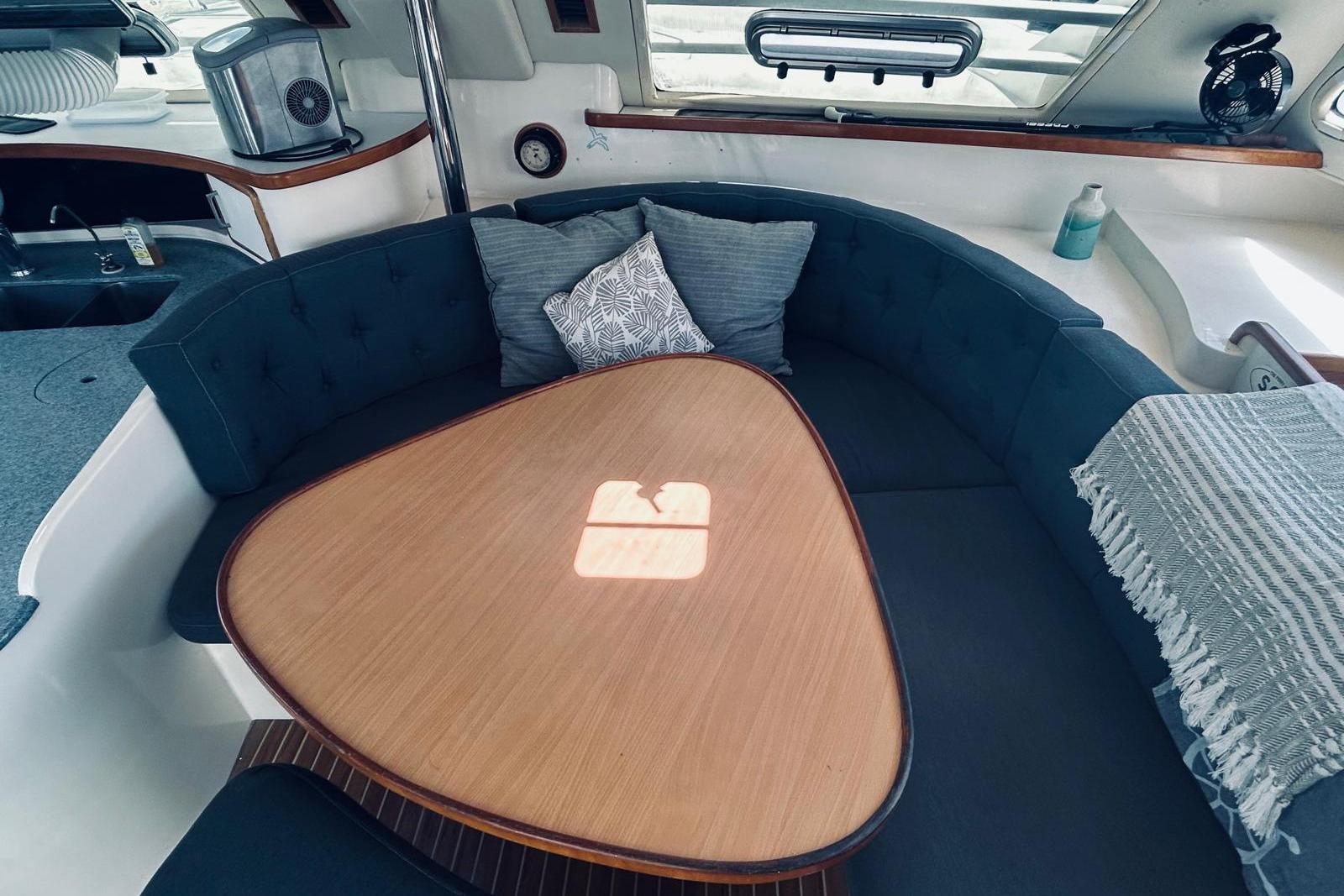 Cozy seating area on 2001 Robertson & Caine Leopard yacht with cushions and wooden table.