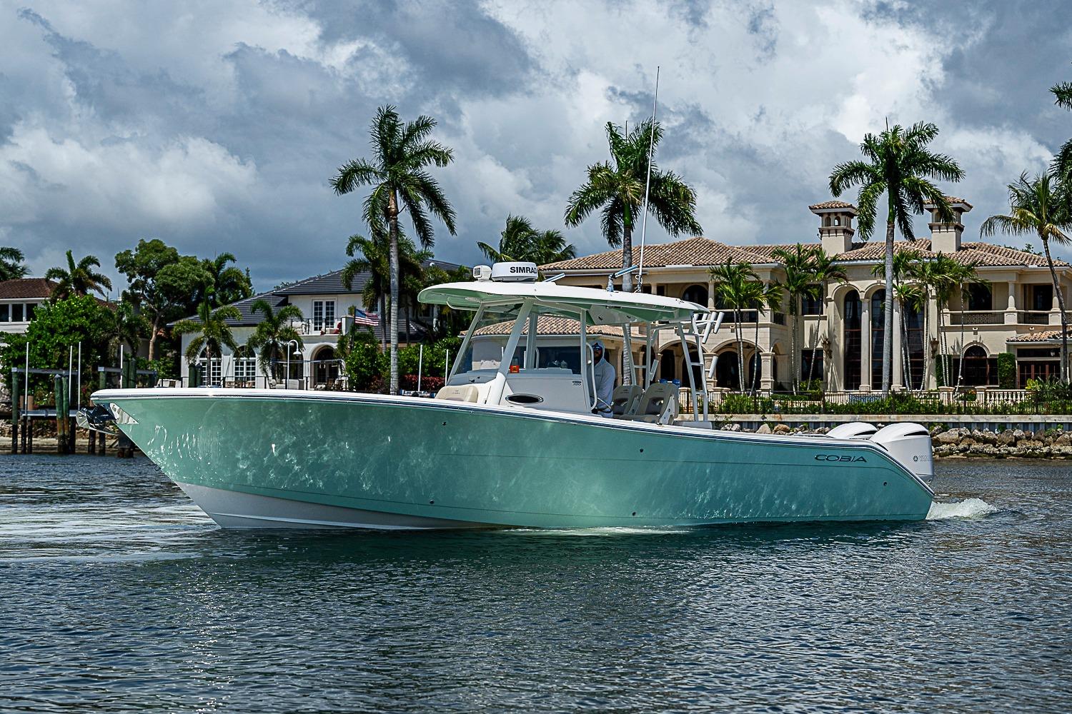 2019 Cobia 320 Center Console boat cruising near luxury waterfront homes.