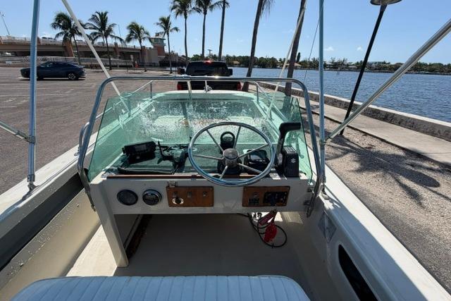 1990 Boston Whaler 17 Newport boat interior with steering wheel, docked near palm trees and water.