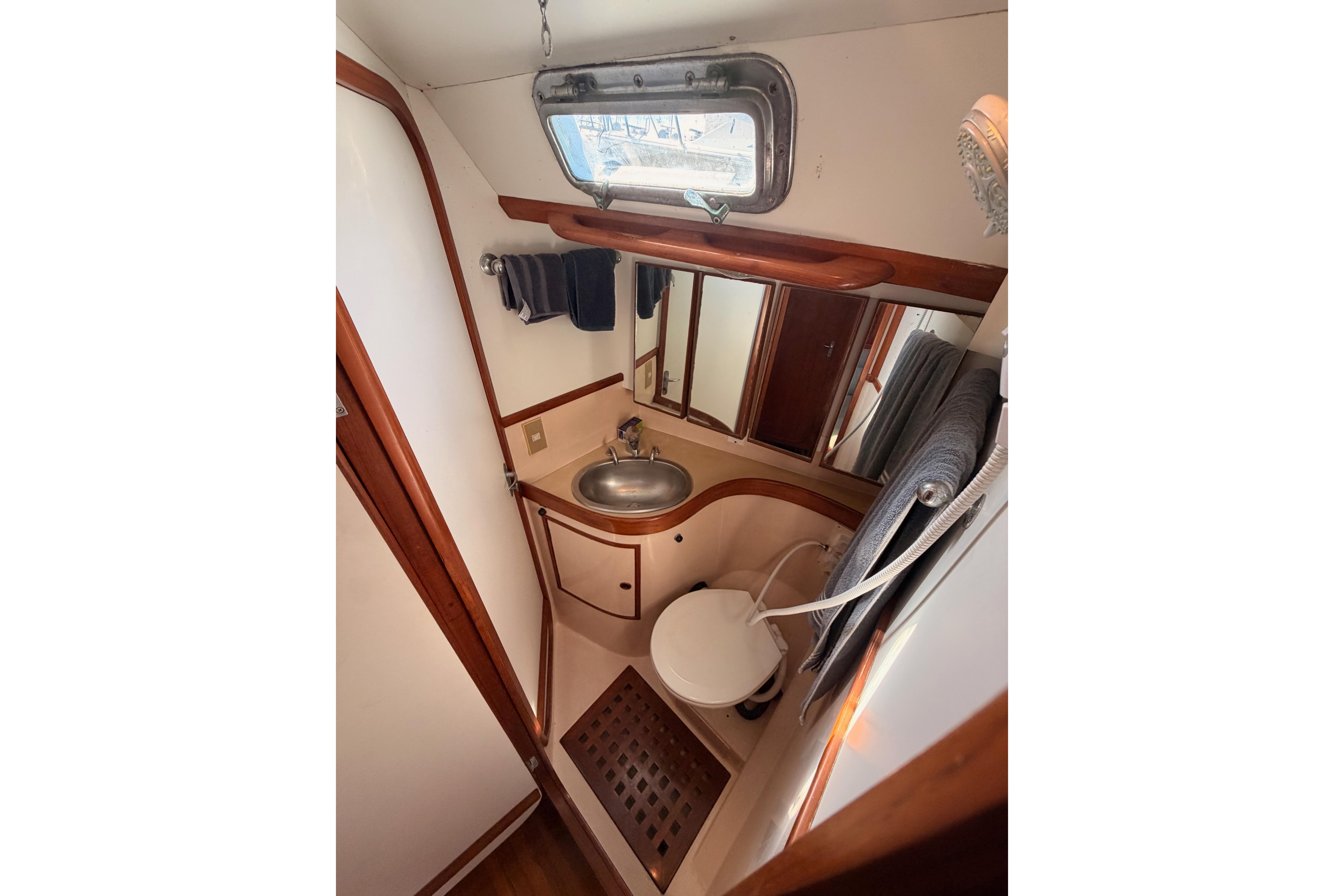 Compact bathroom in a 1991 Hylas 51 yacht with sink, toilet, and porthole window.