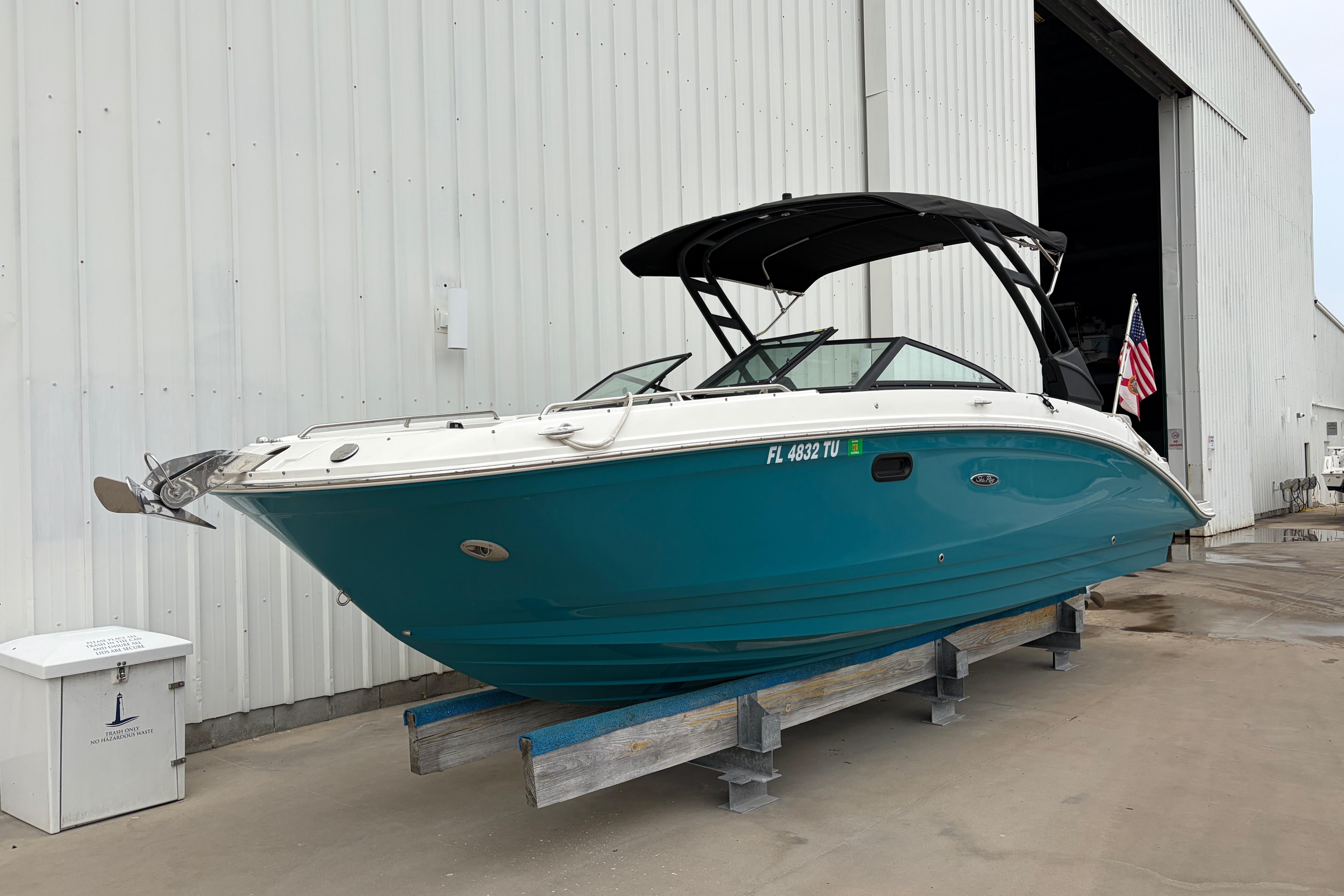 2024 Sea Ray SDX 270 Outboard boat in teal, docked near a large warehouse.