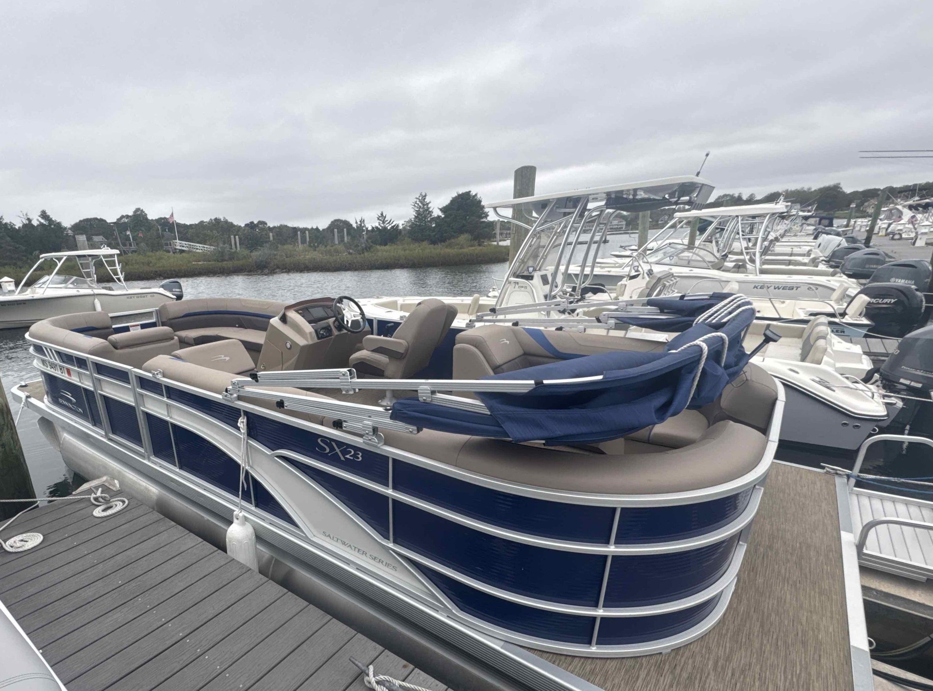 A 2023 Bennington 23SXSRC pontoon boat docked. It features blue and beige upholstery.