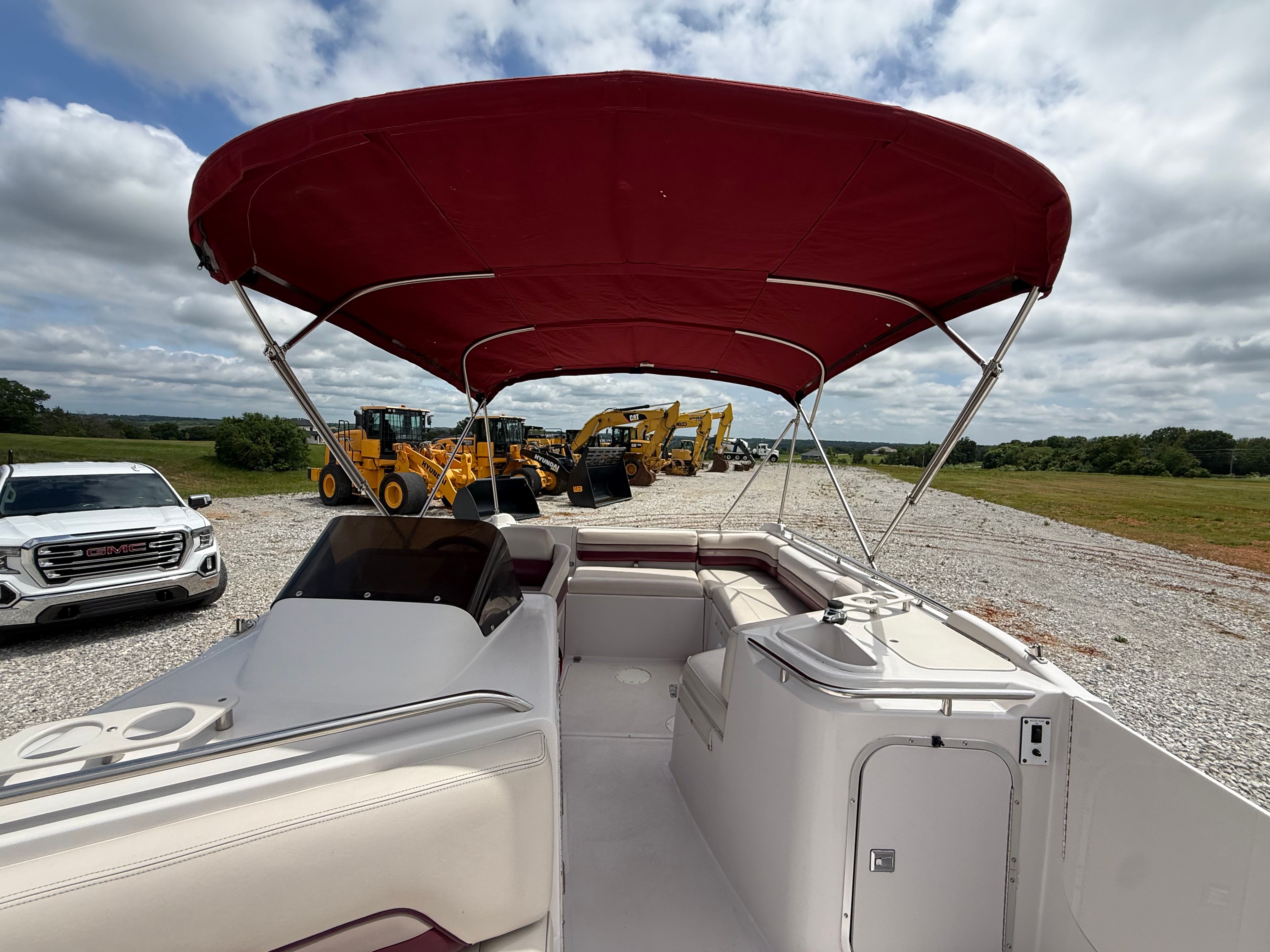 A 1994 Chaparral Sunesta 220 with a red canopy, parked on gravel next to construction equipment.