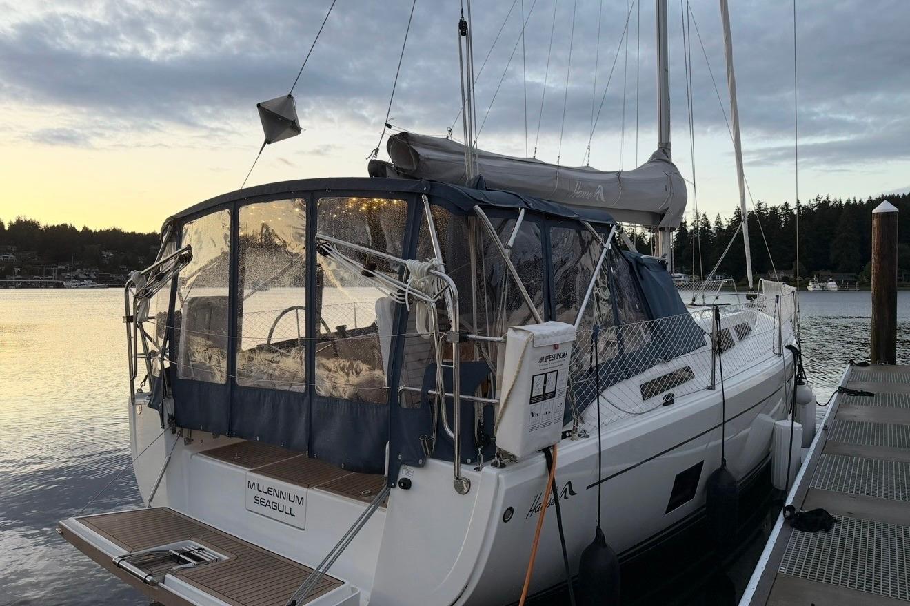2022 Hanse 418 sailboat docked at sunset, featuring covered cockpit and serene water backdrop.