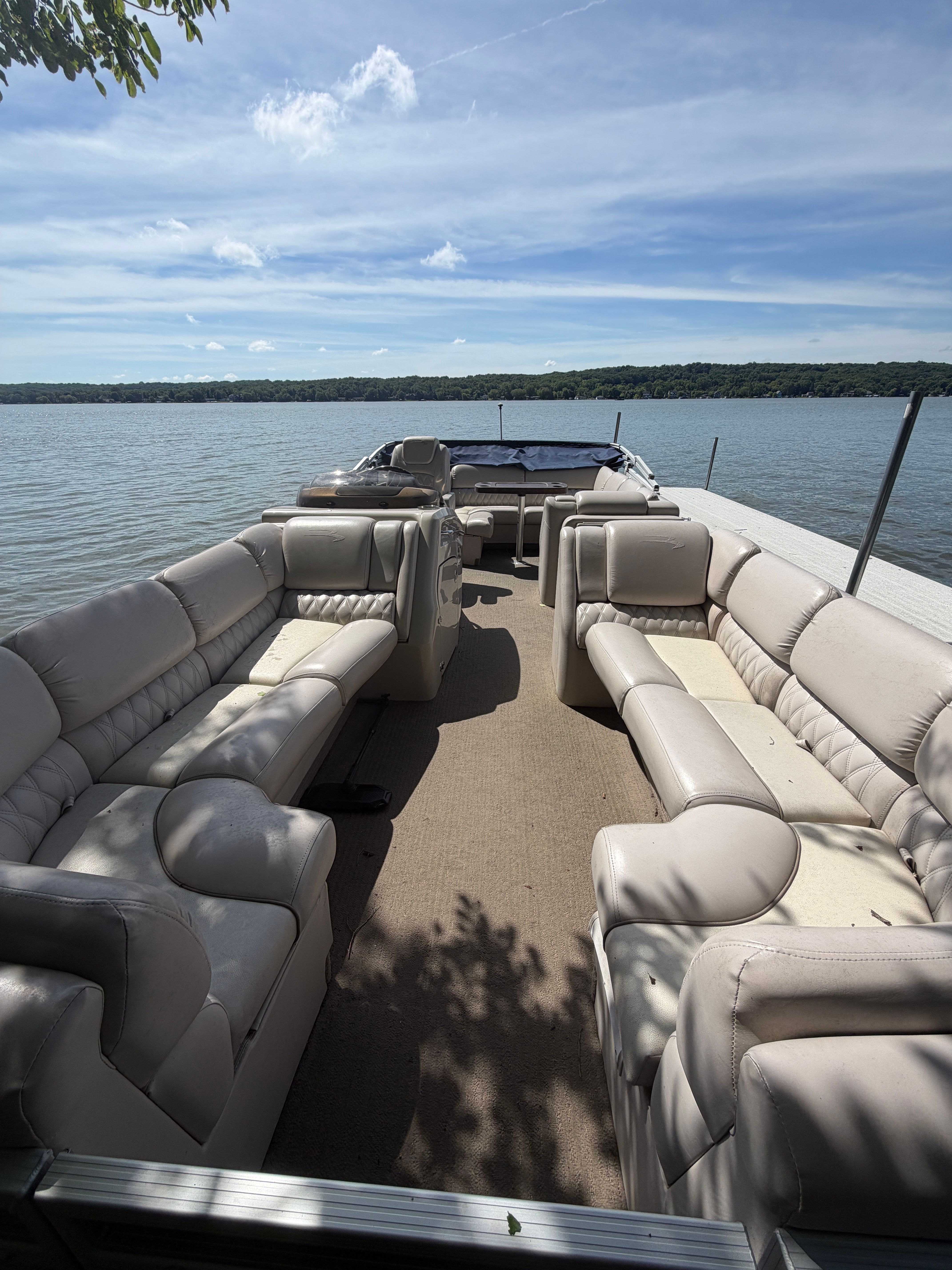 Interior view of a Bennington 2350 RCL pontoon boat with beige seating on a calm lake.