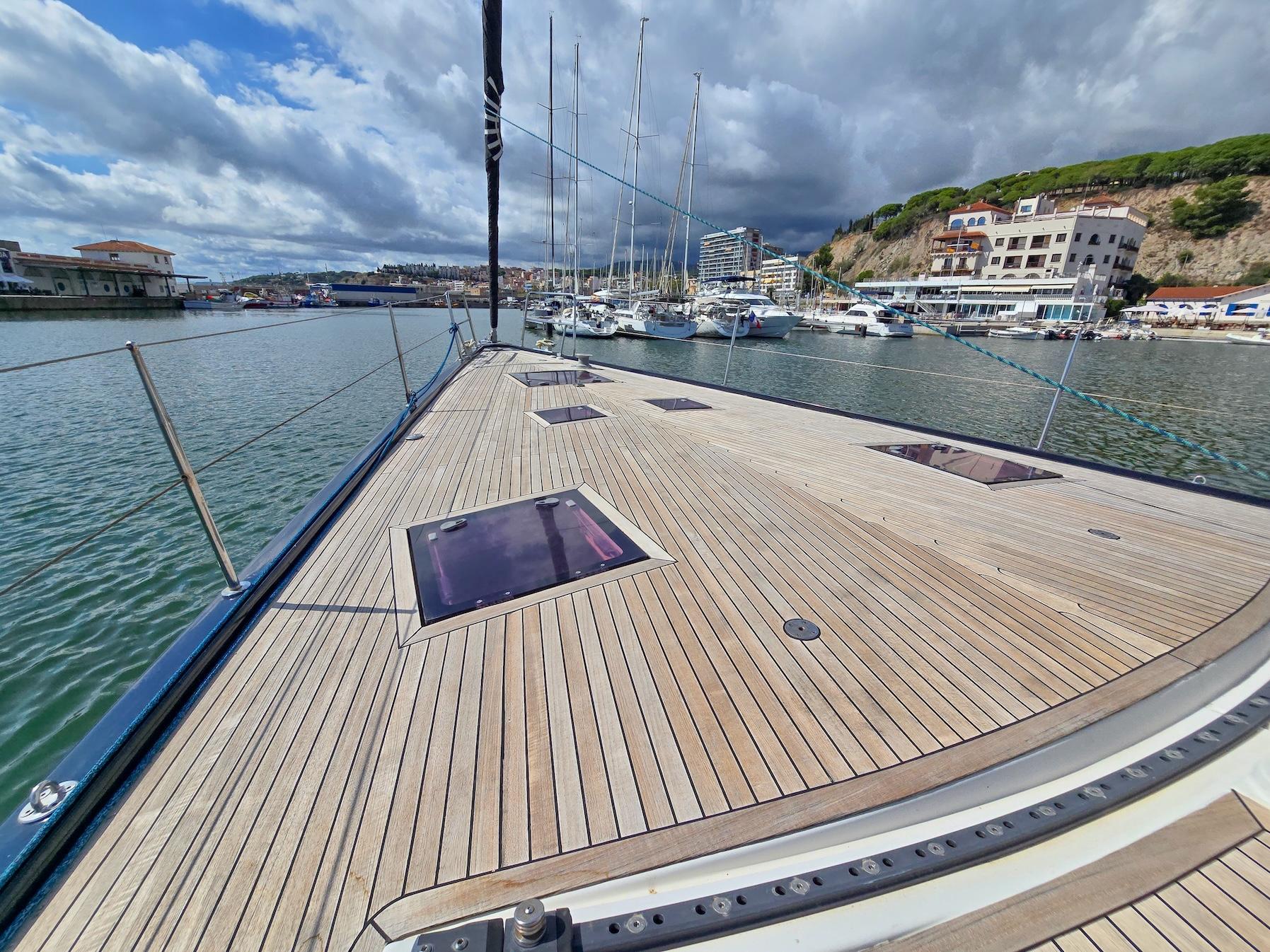 2009 Hanse 630e yacht deck in marina, clear sky, calm water, coastal buildings.