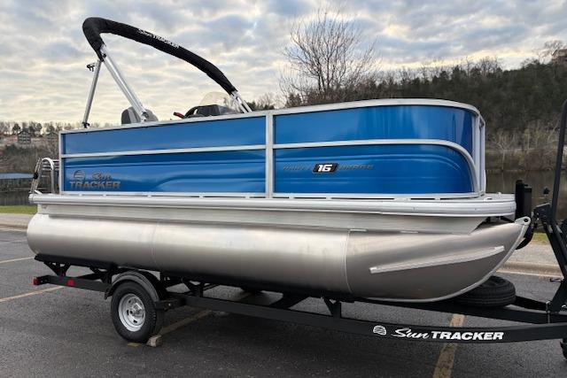 2026 Sun Tracker Party Barge 16 DLX pontoon boat on trailer, blue and silver design.