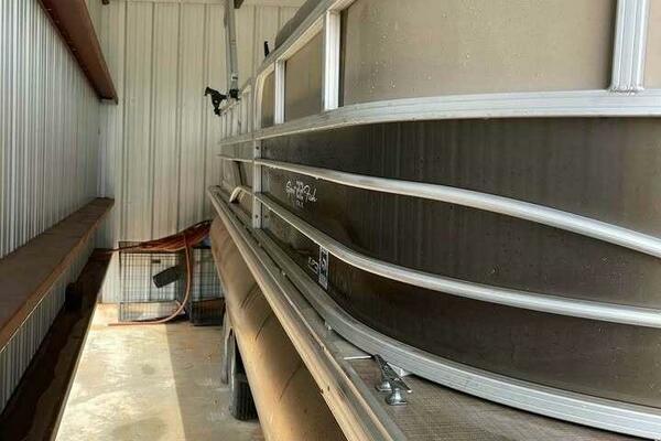 2019 Sun Tracker SportFish 22 DLX pontoon boat stored in a metal shed.