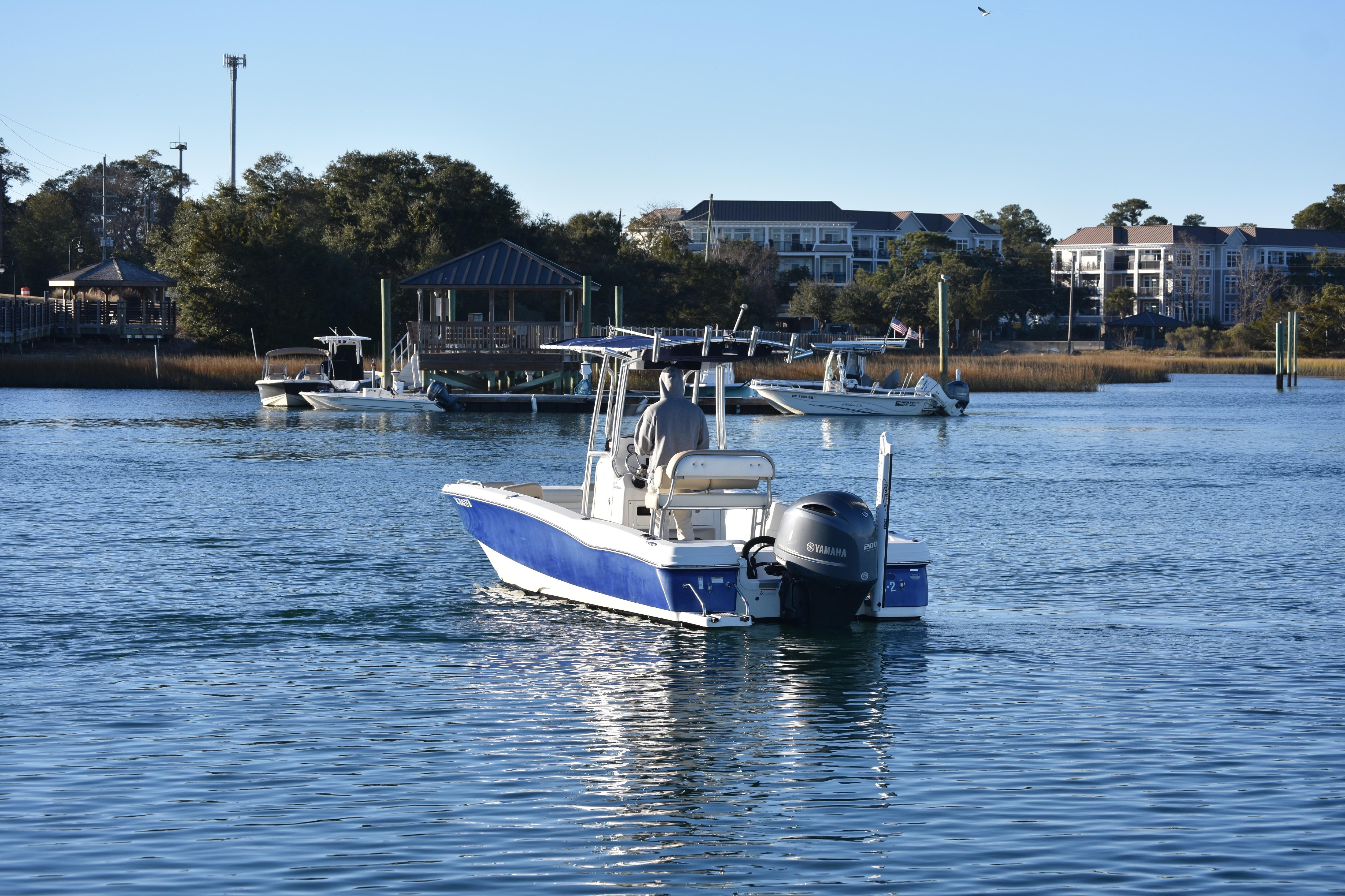 2017 NauticStar 231 Angler boat on calm water near a marina with buildings in the background.