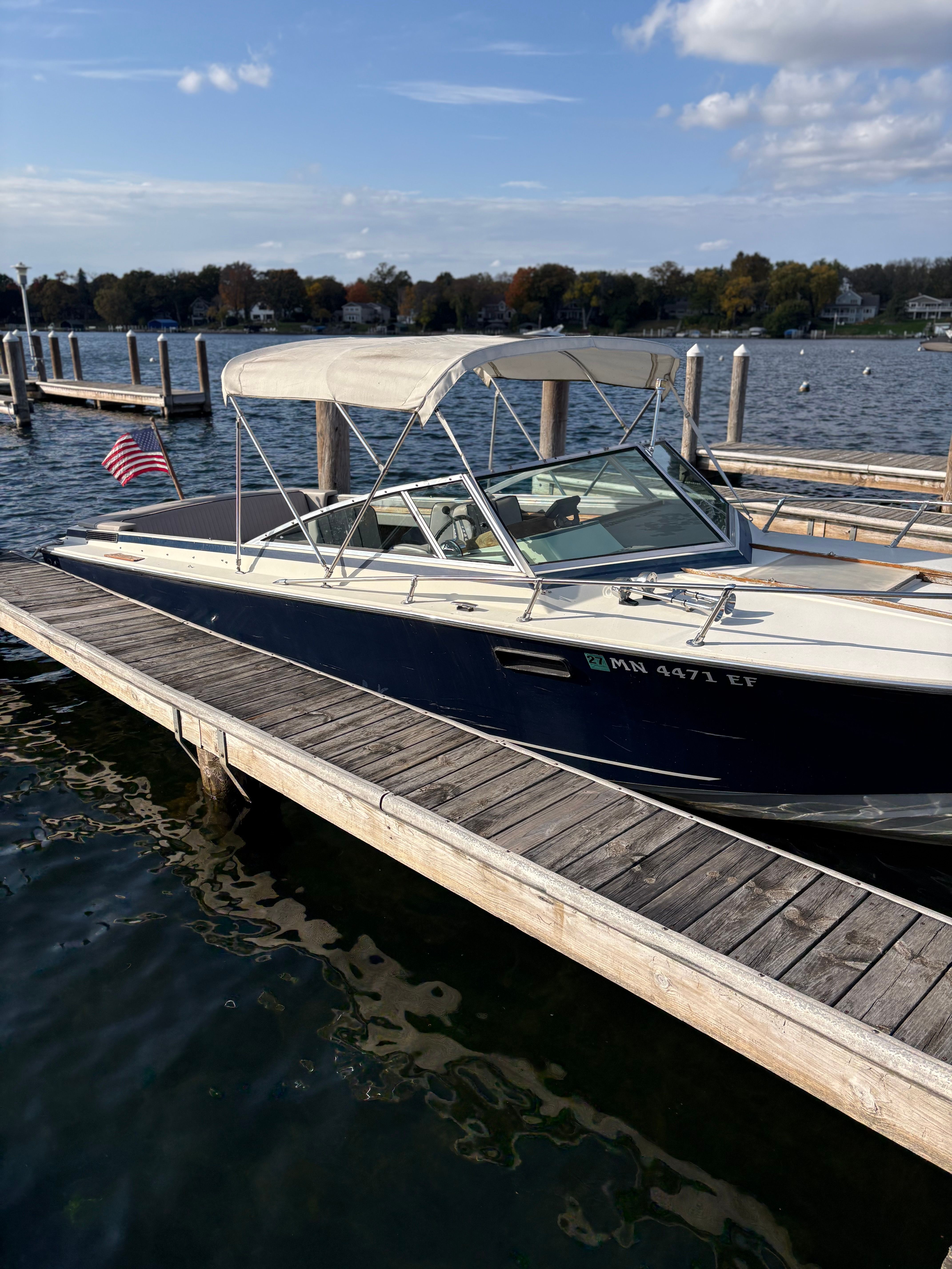 A blue and white boat with a canopy docked at a wooden pier on the water.