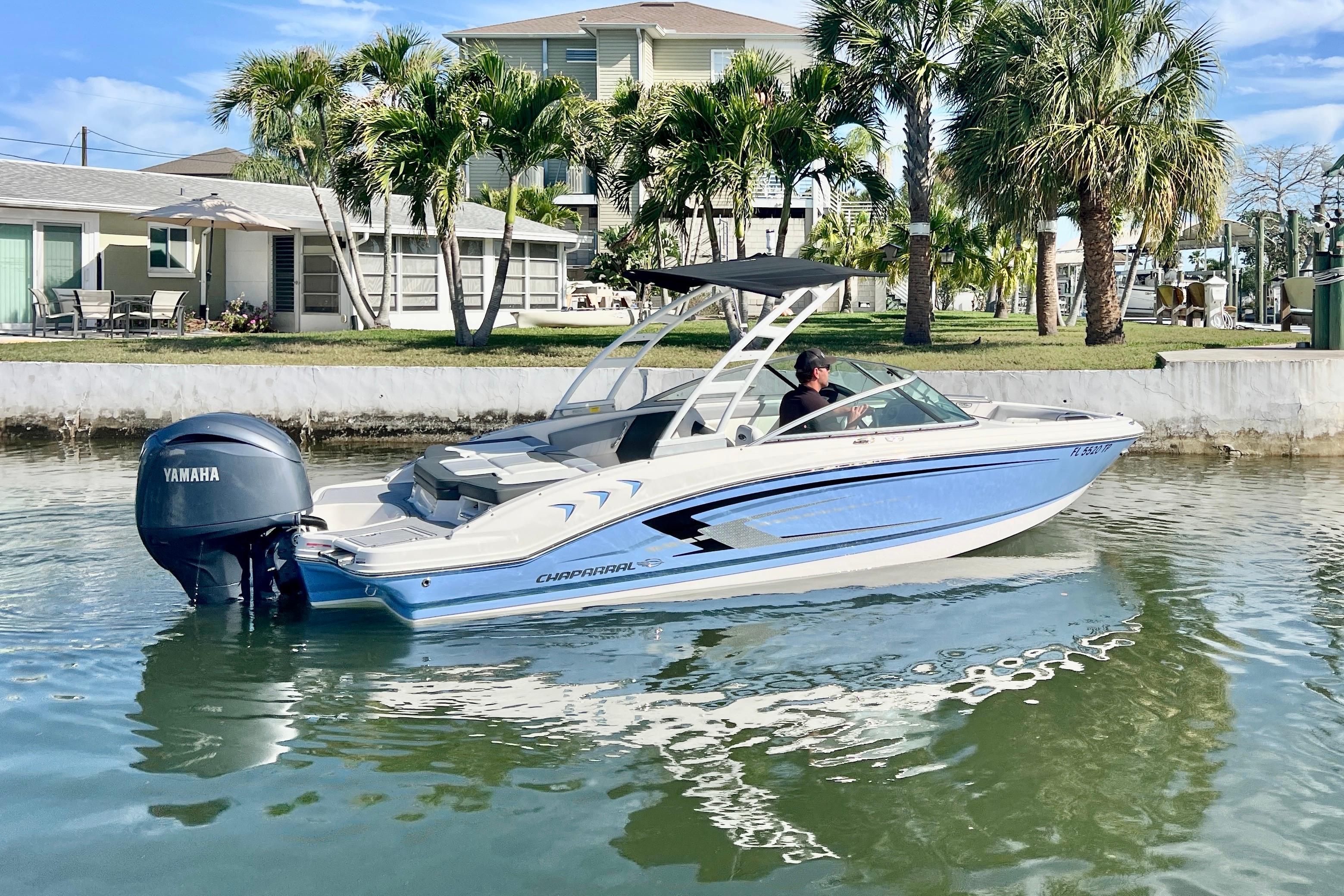2023 Chaparral 21 SSi OB boat cruising on a sunny waterfront with palm trees.