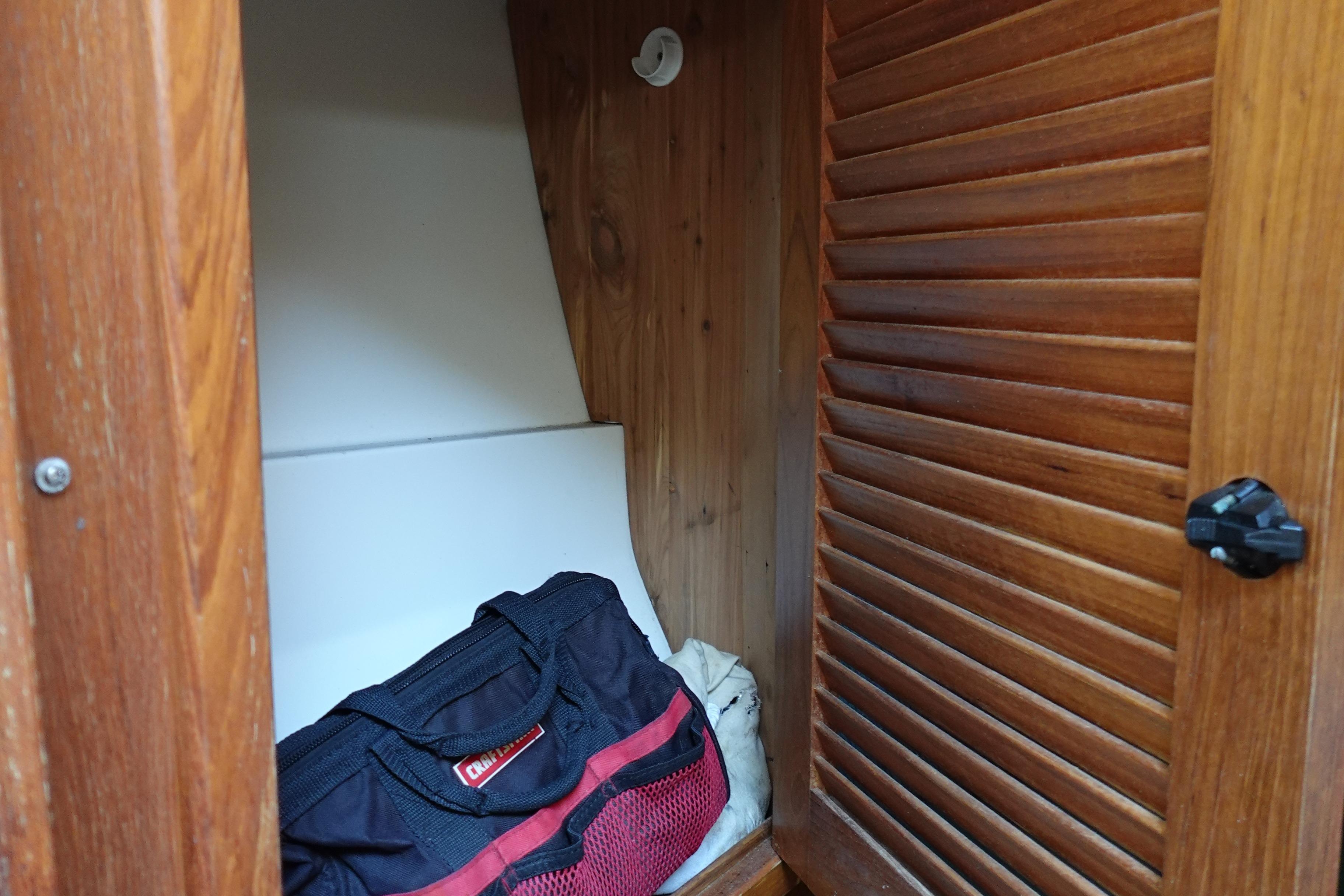 Wooden cabinet interior with a black and red bag inside a 1997 Catalina 28 sailboat.