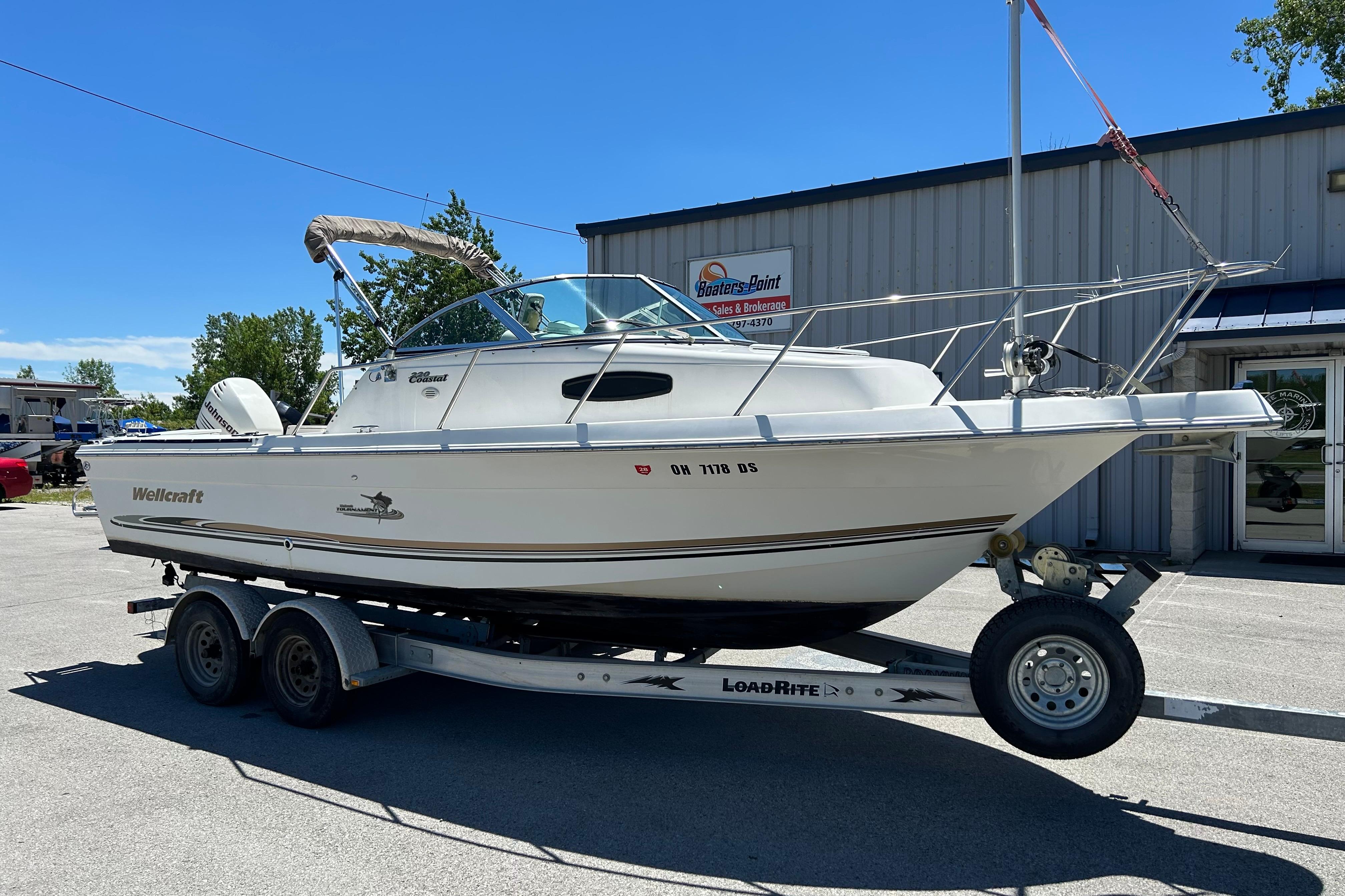 2003 Wellcraft 220 Coastal boat on trailer, parked outside dealership under clear blue sky.